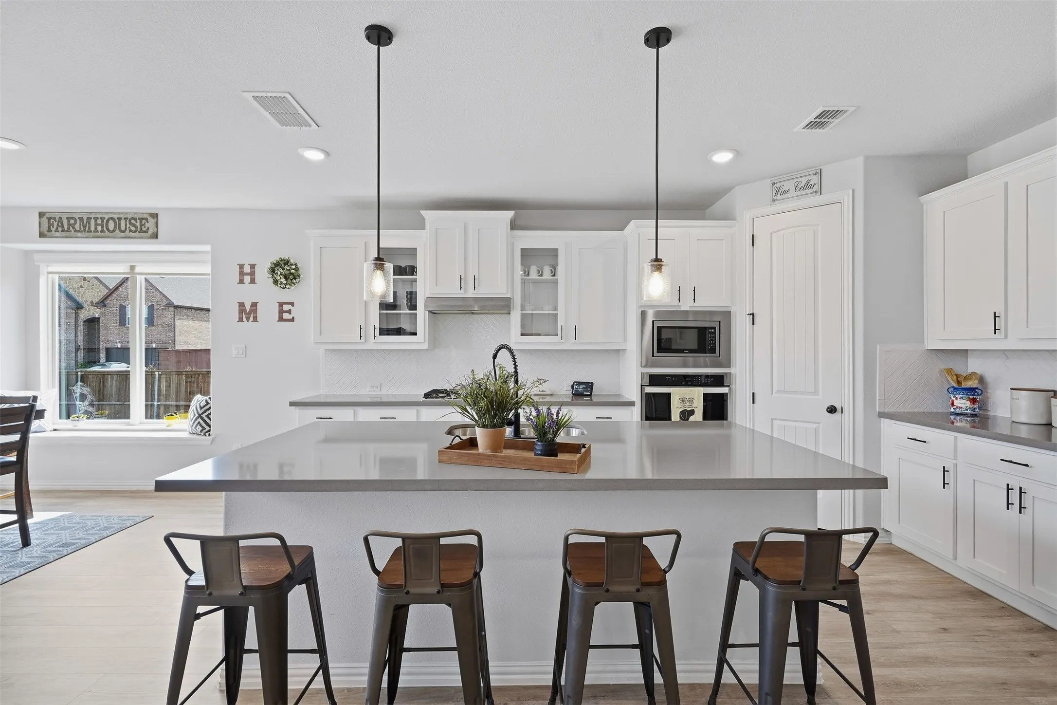 Kitchen featuring a large island with pendant lighting, white cabinetry, integrated stainless steel microwave, and wood-finish flooring