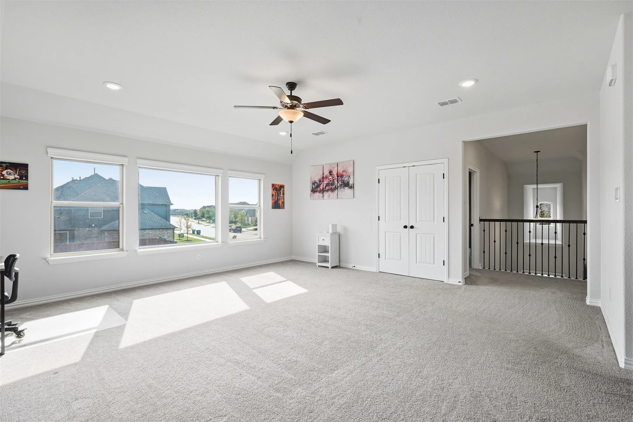 Spacious carpeted room featuring multiple windows, recessed lighting, ceiling fan, and double panel doors