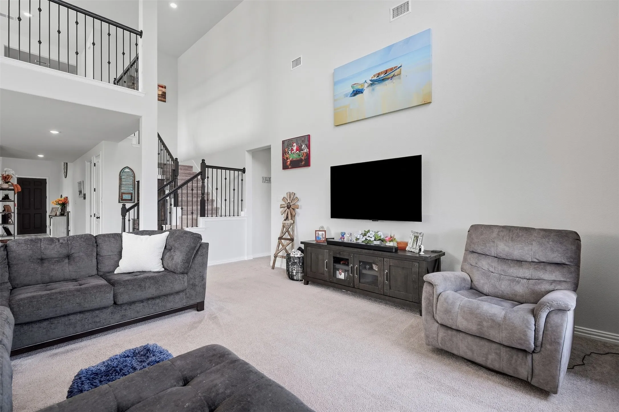 Two-story living area with high ceilings, carpeted flooring, and a media console