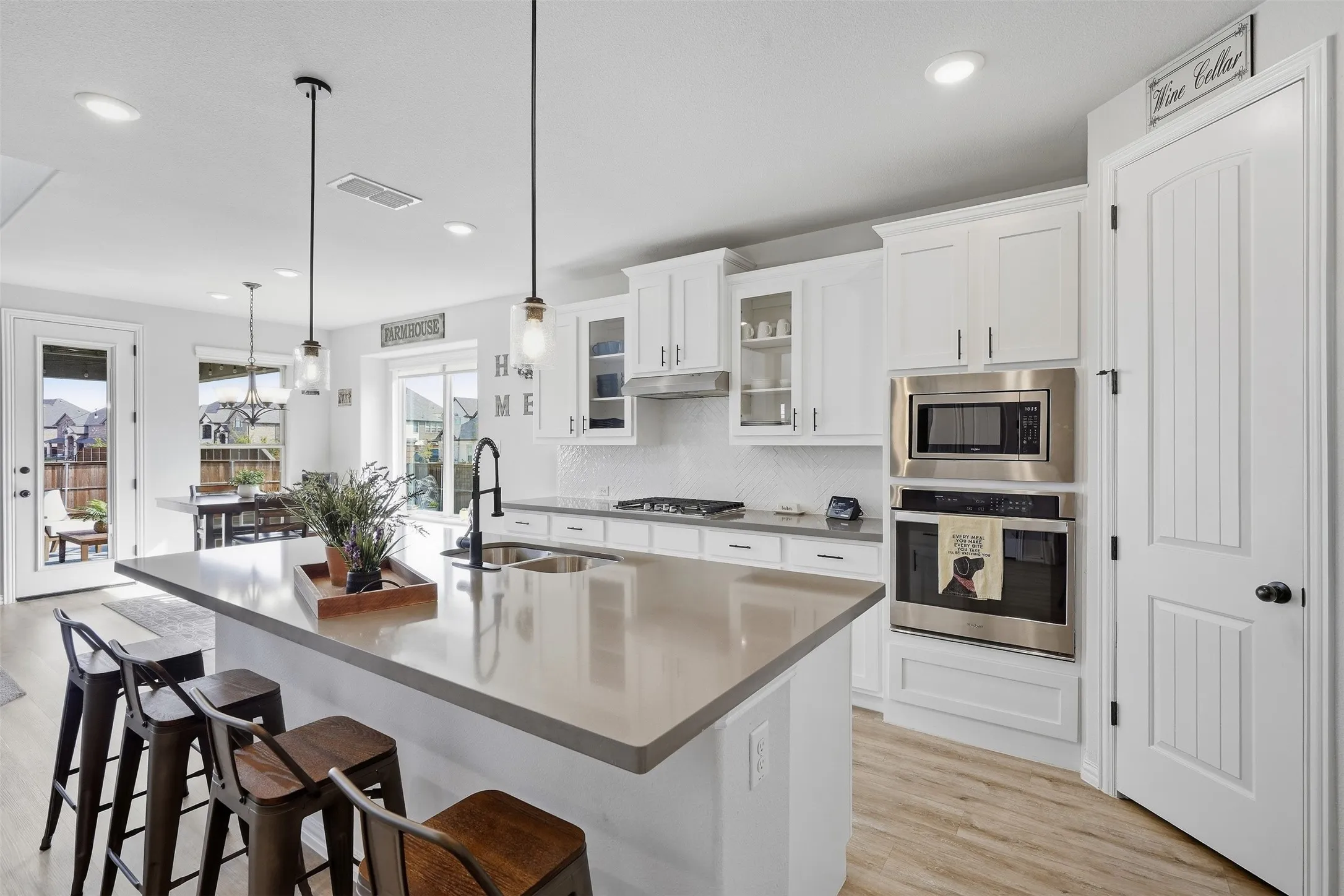 White cabinetry, stainless steel appliances, solid surface countertops, wood-finish flooring, and pendant lighting