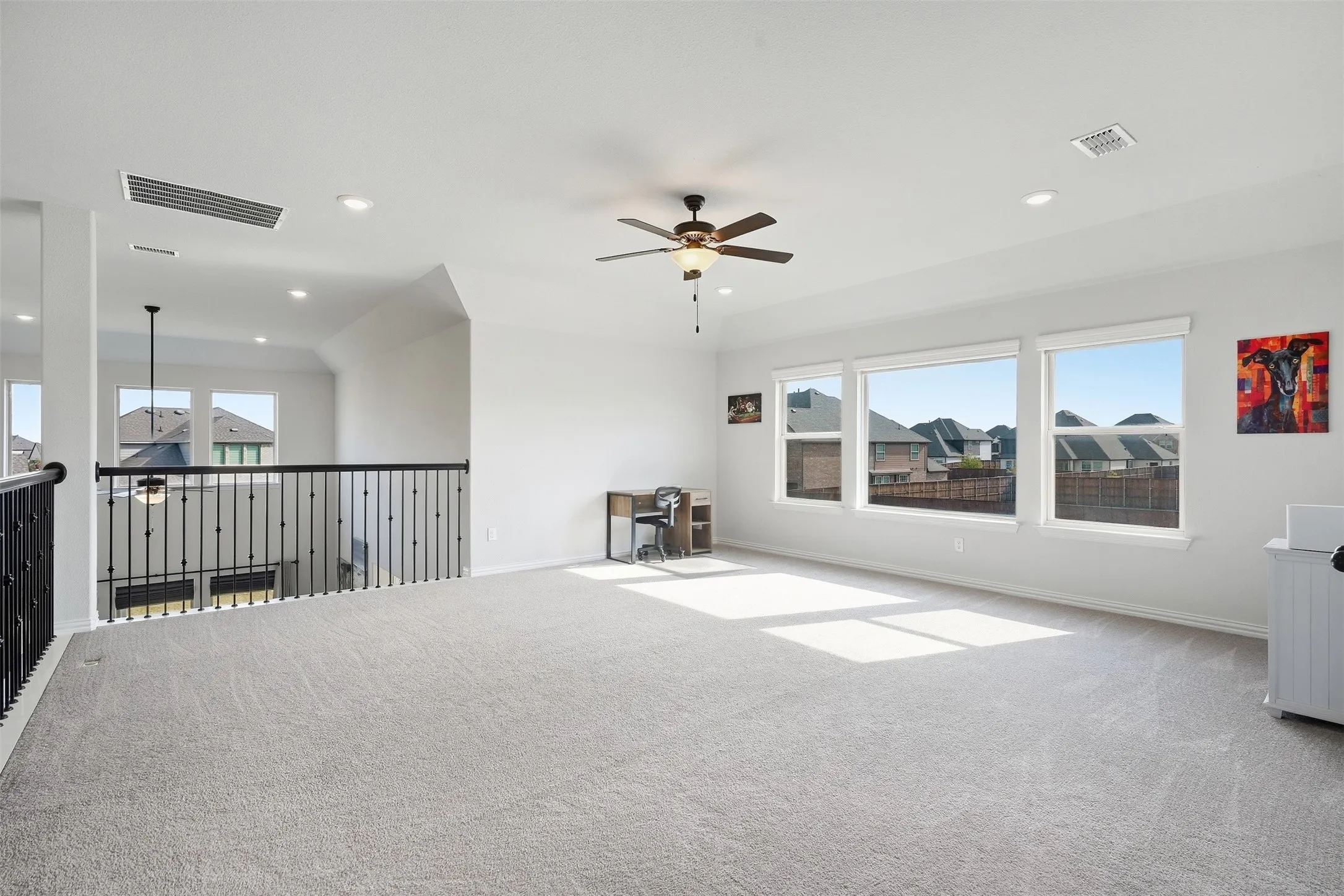 Spacious carpeted room featuring a ceiling fan, recessed lighting, and multiple windows