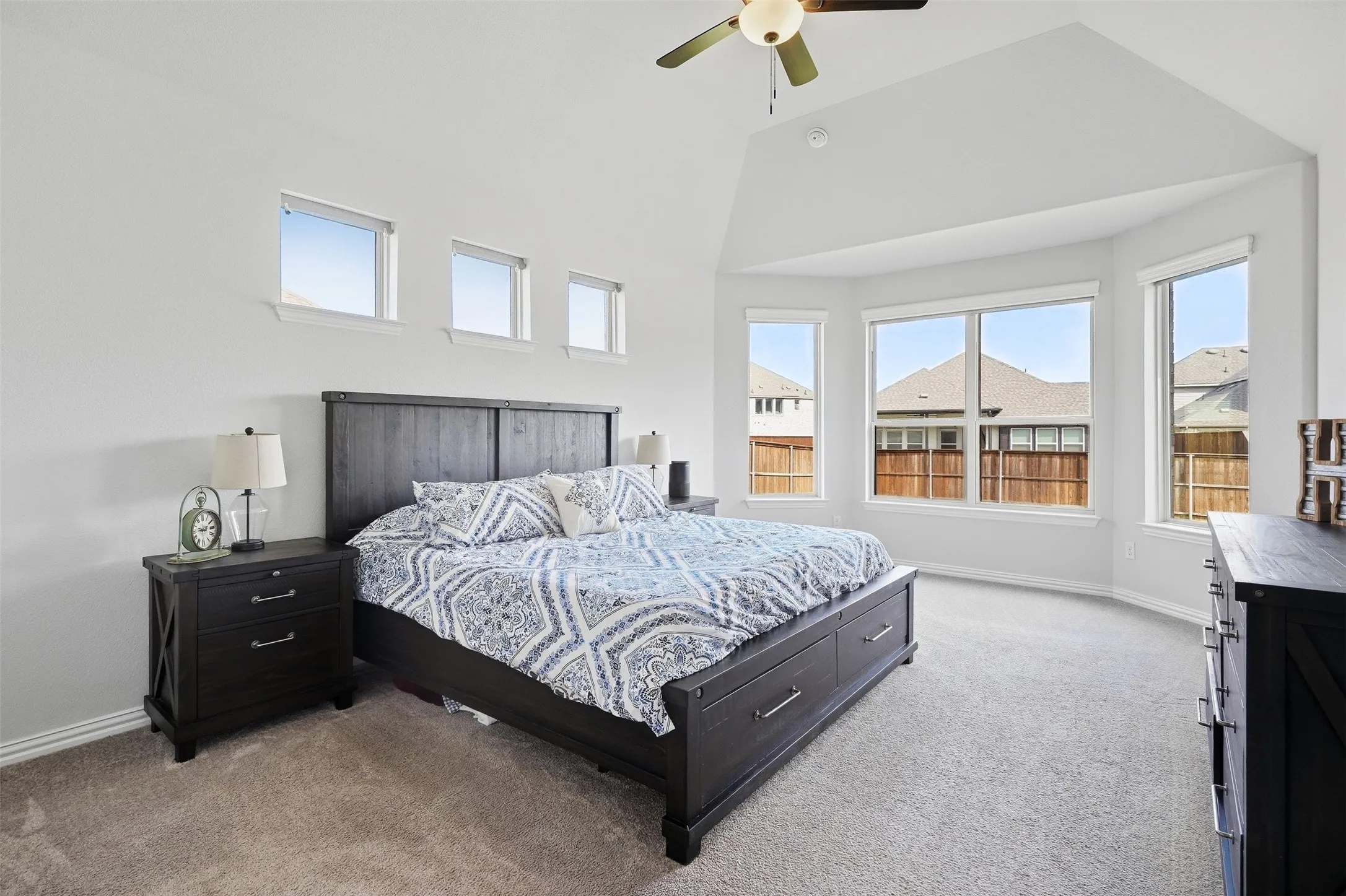 Vaulted ceiling with a ceiling fan, bay window configuration, high transom windows, and carpet flooring