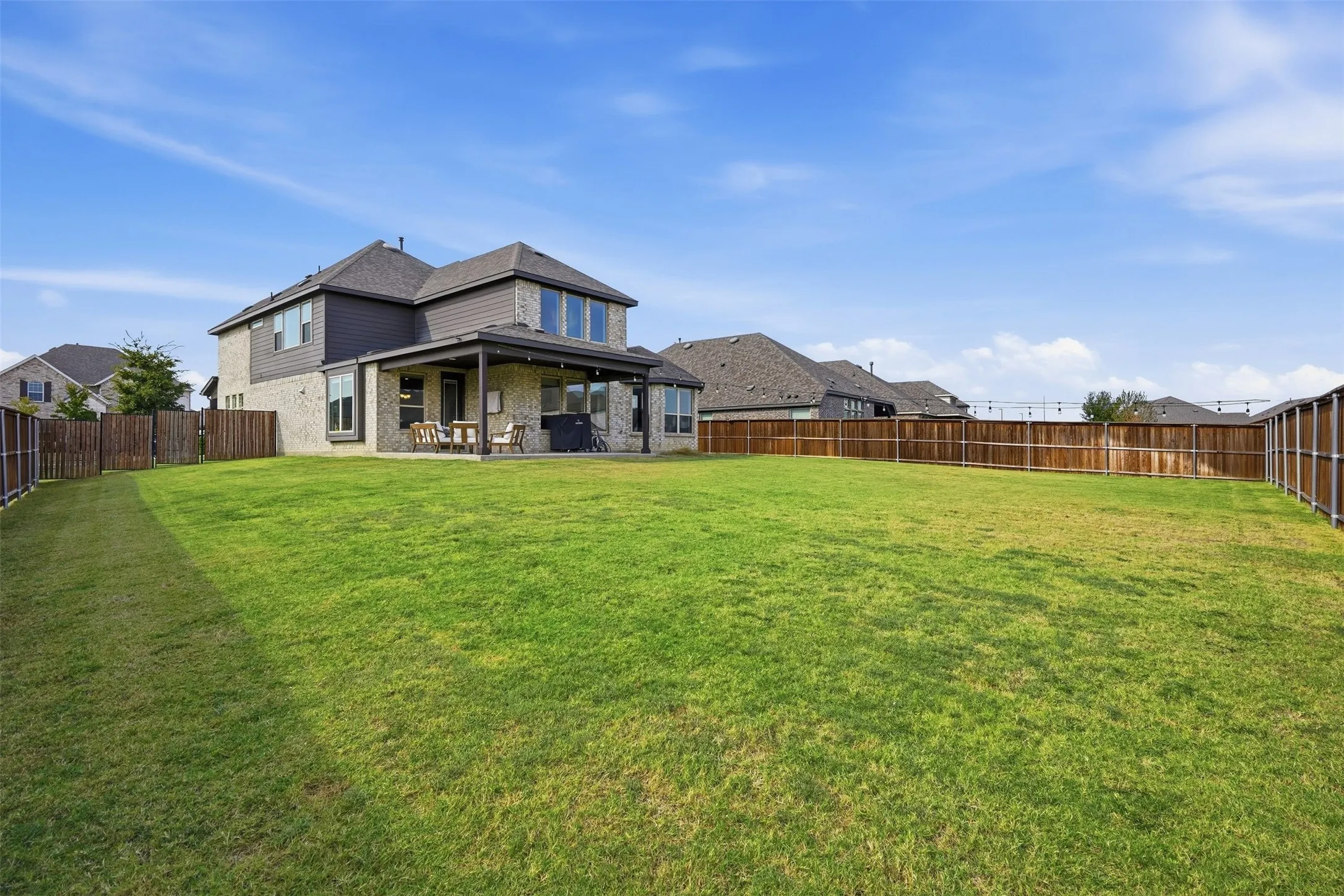 Expansive backyard with a covered patio, wood privacy fencing, and a two-story residence with brick and siding exterior
