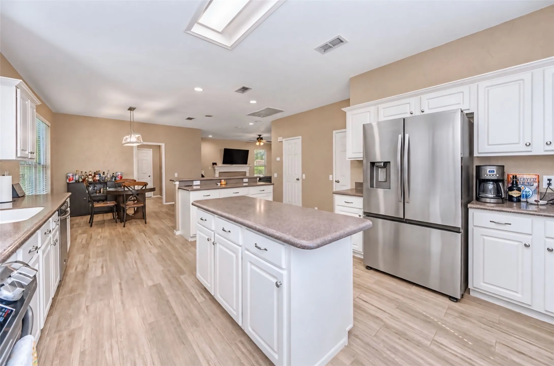 Spacious kitchen featuring white cabinetry, a large center island, stainless steel appliances, wood-finish flooring, and a ceiling skylight