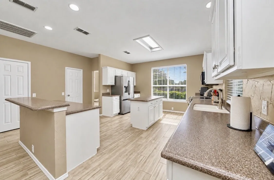 Kitchen featuring wood-finish flooring, white cabinetry, a skylight, and stone-finish countertops