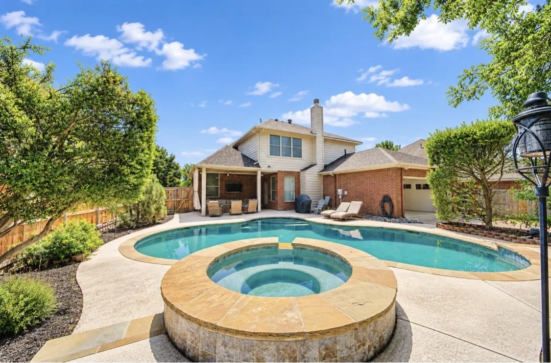 Expansive backyard featuring a curved swimming pool, integrated spa with stone coping, and a concrete patio