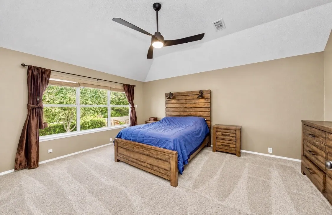Vaulted ceiling with an attached ceiling fan, expansive window, neutral wall tones, and light-toned carpet flooring