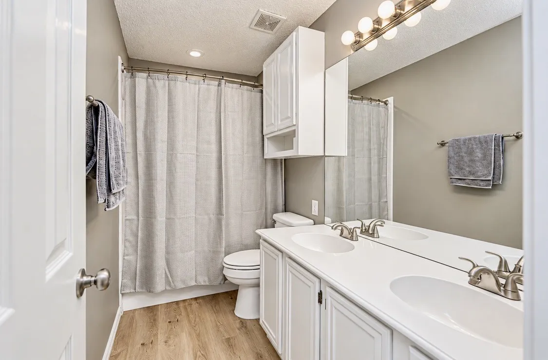 Dual sink vanity, brush nickel fixtures, wood-finish flooring, recessed lighting, and wall-mounted storage