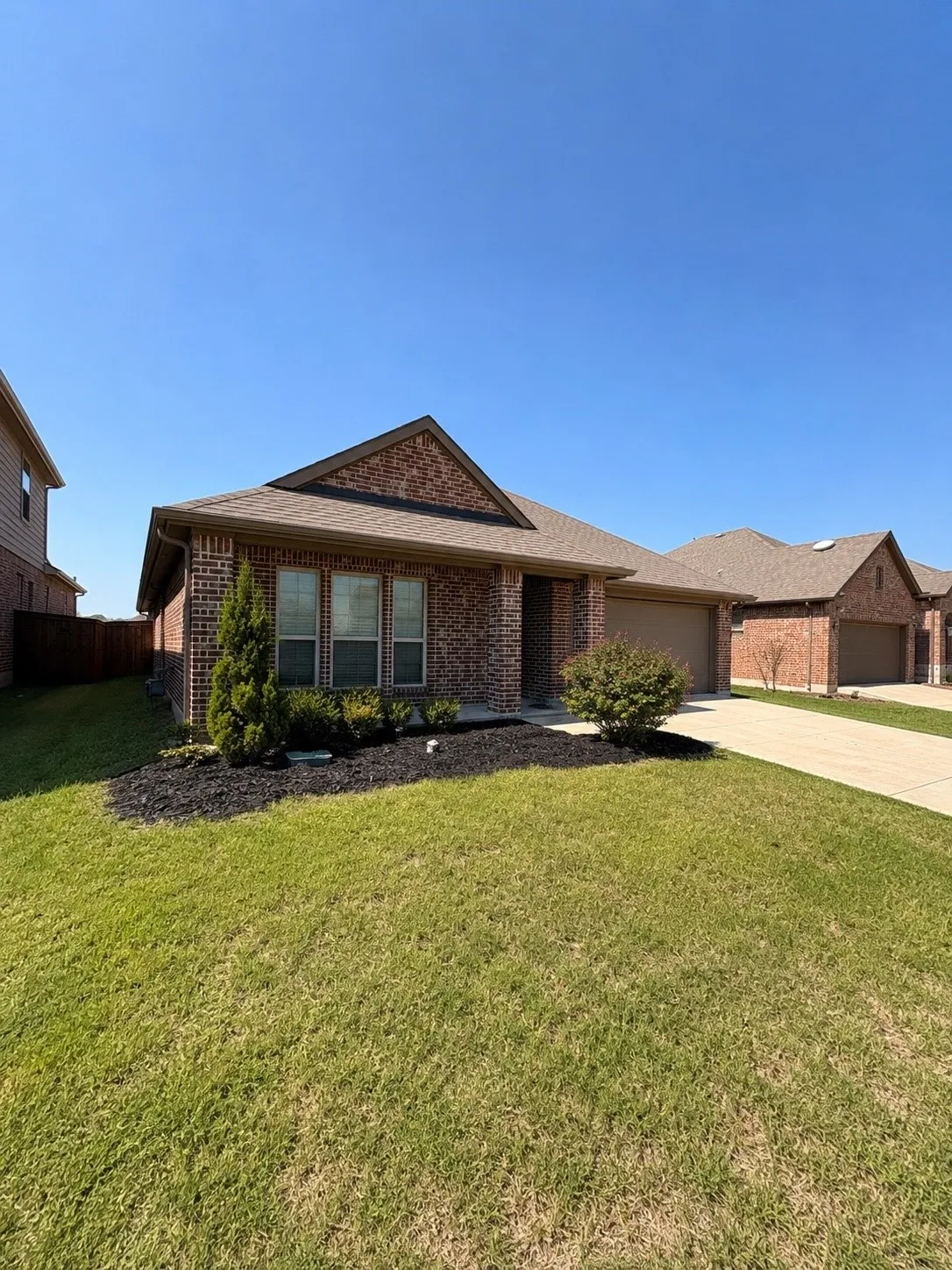Brick exterior with gabled roofline, attached two-car garage, concrete driveway, and front lawn with landscaping