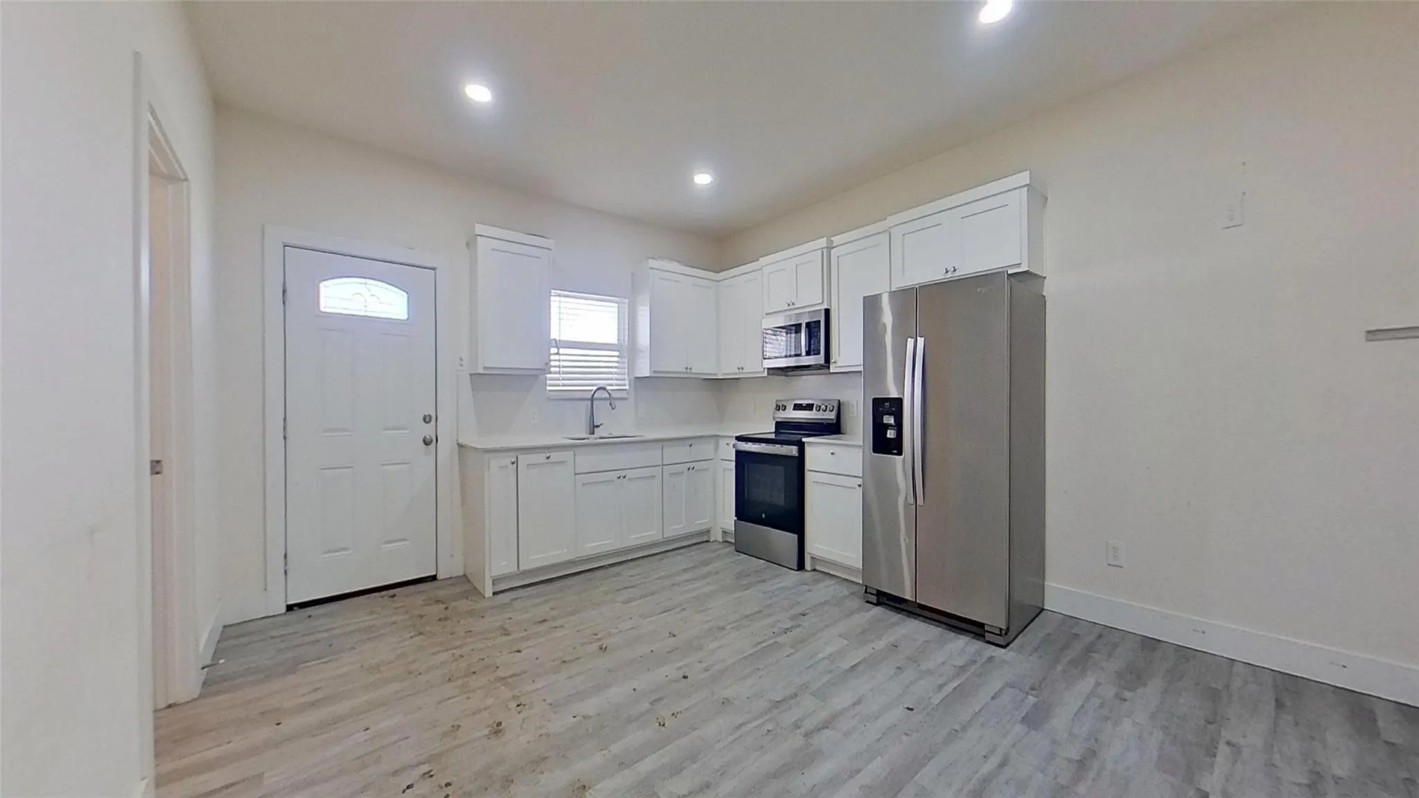 Kitchen featuring white cabinetry, stainless steel appliances, light-toned countertops, wood-finish flooring, and recessed lighting