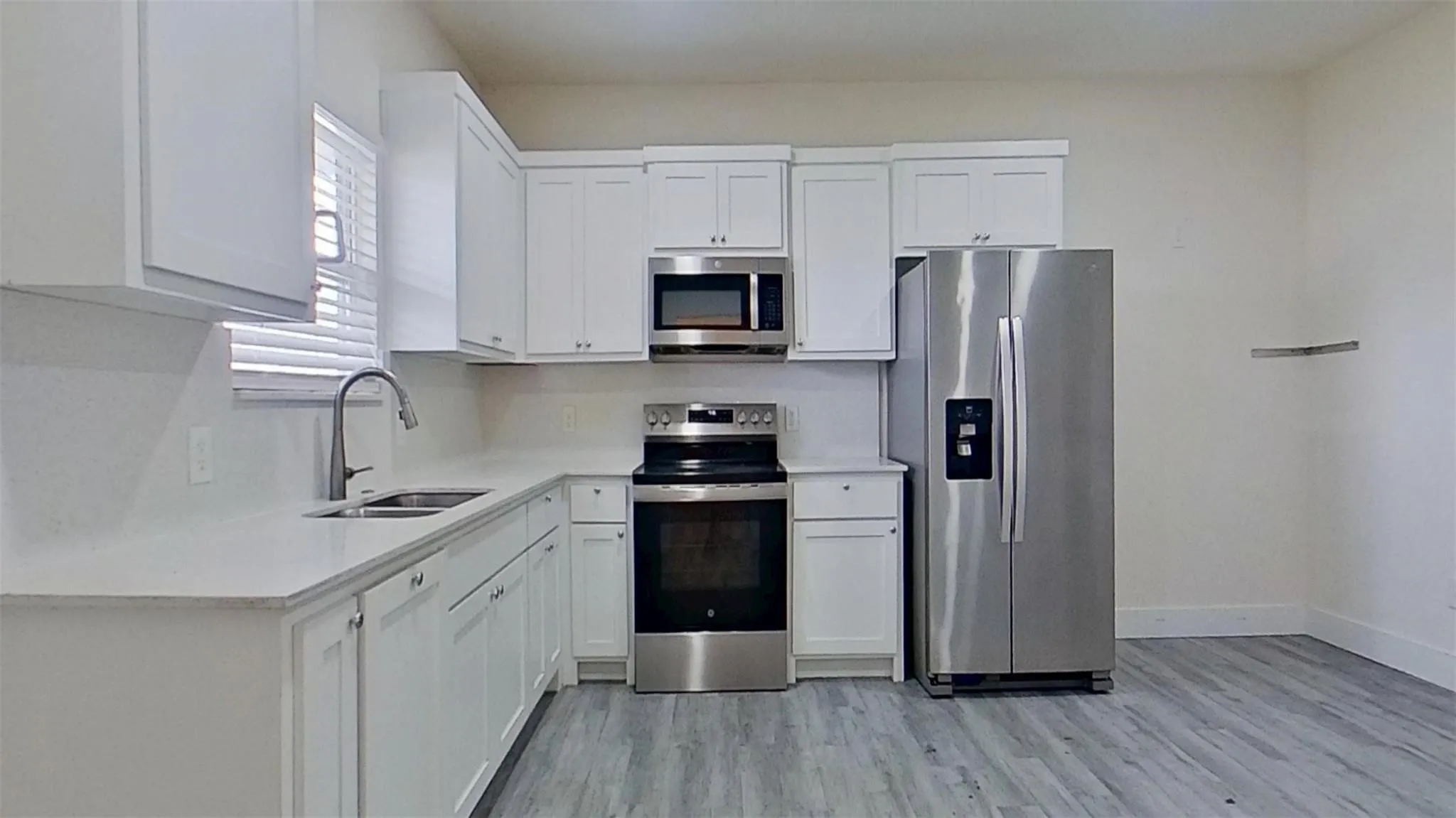 Kitchen with white shaker cabinetry, stainless steel appliances, light-toned countertops, and wood-finish flooring