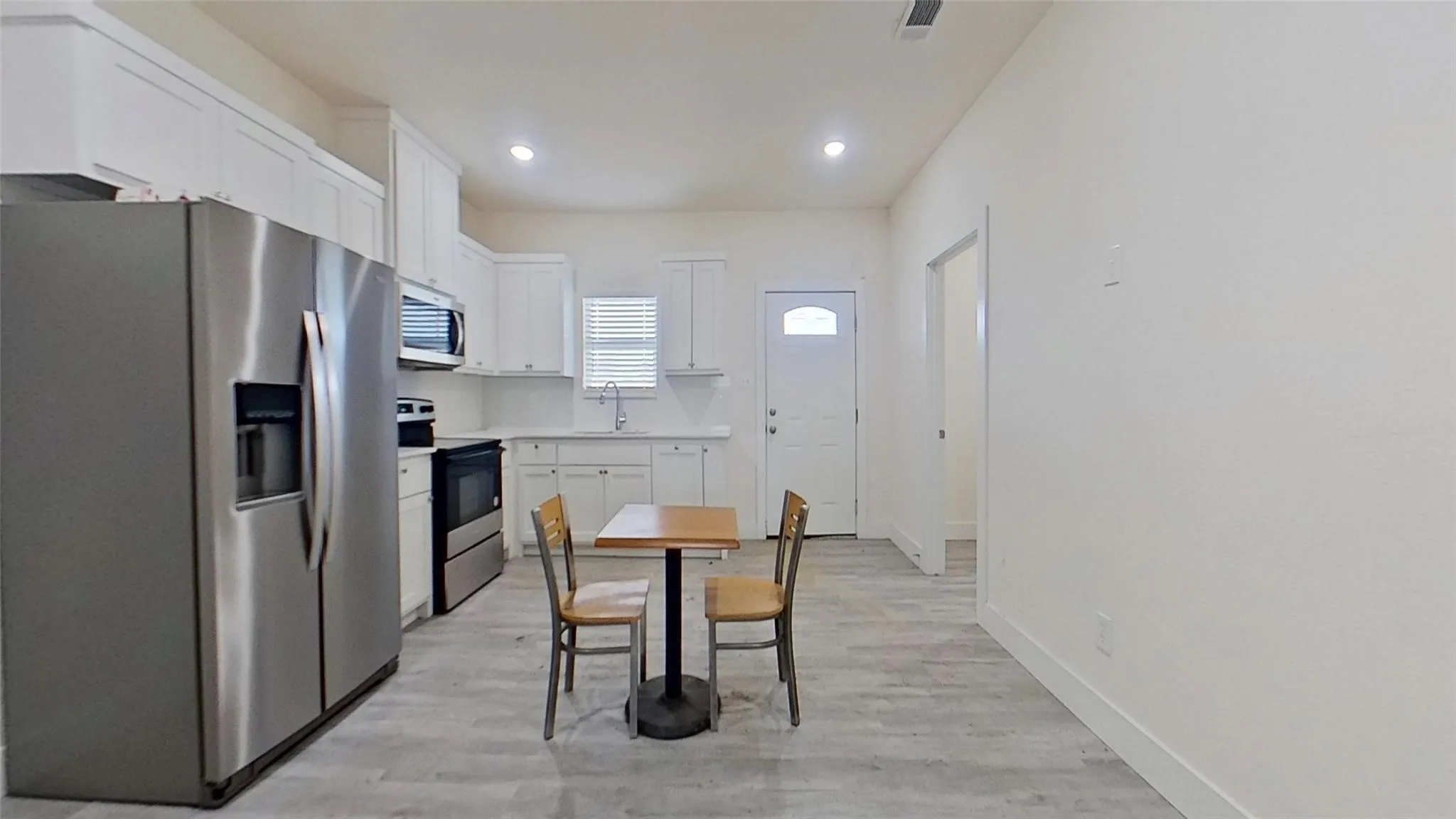 Kitchen with stainless steel appliances, white cabinetry, integrated sink, and wood-finish flooring