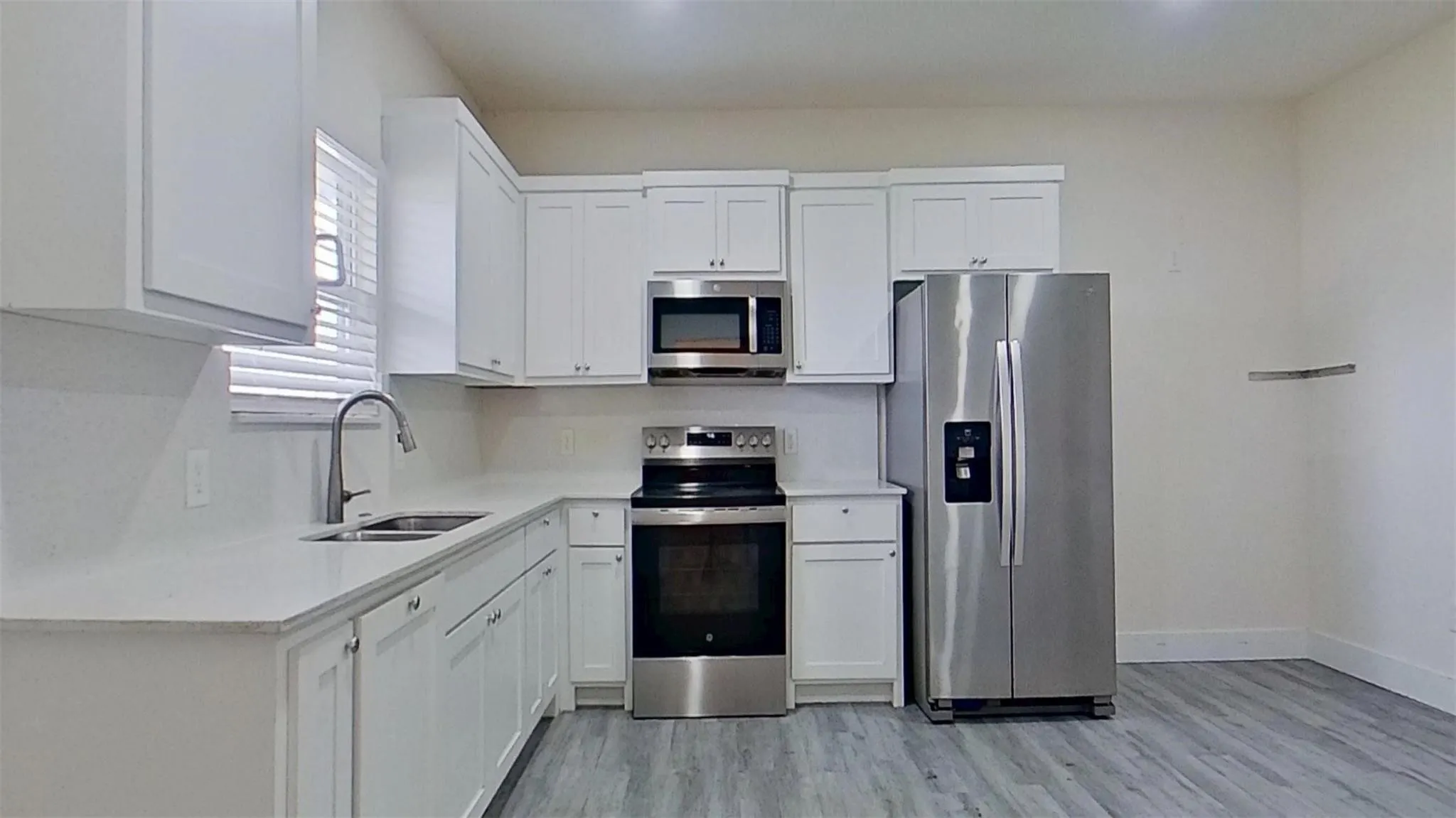 Kitchen featuring white cabinetry, light-toned countertops, stainless steel appliances, and wood-finish flooring