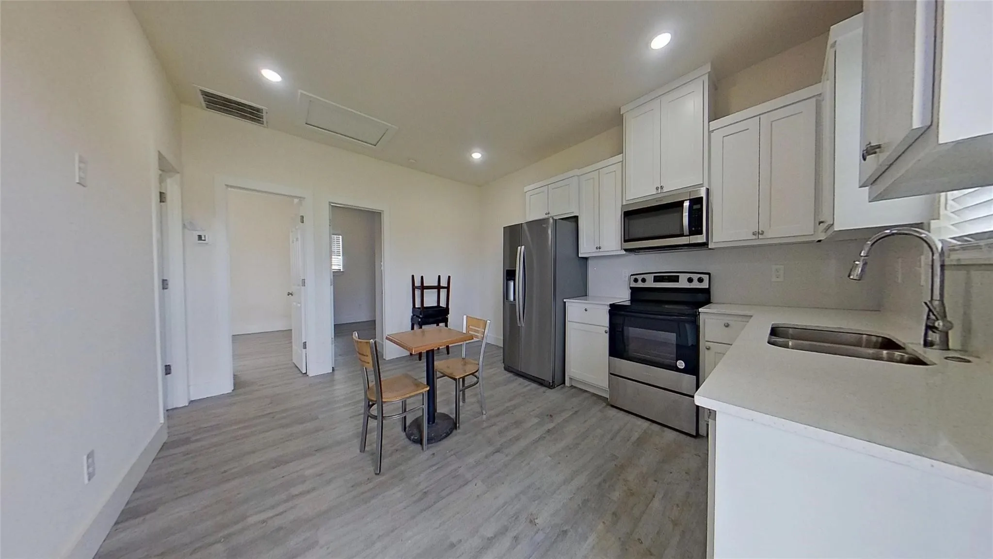 Kitchen featuring stainless steel appliances, white cabinetry, a stainless steel sink, light-toned countertops, and wood-finish flooring