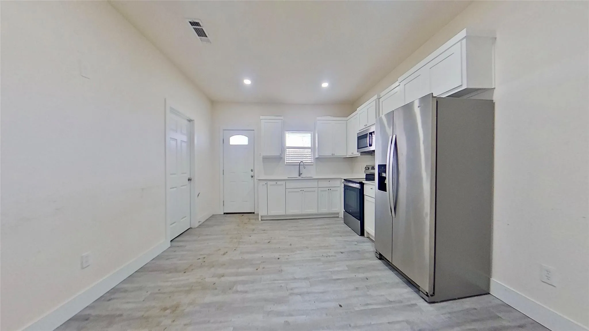Light wood-finish flooring, recessed lighting, white cabinetry, stainless steel appliances, and white countertops