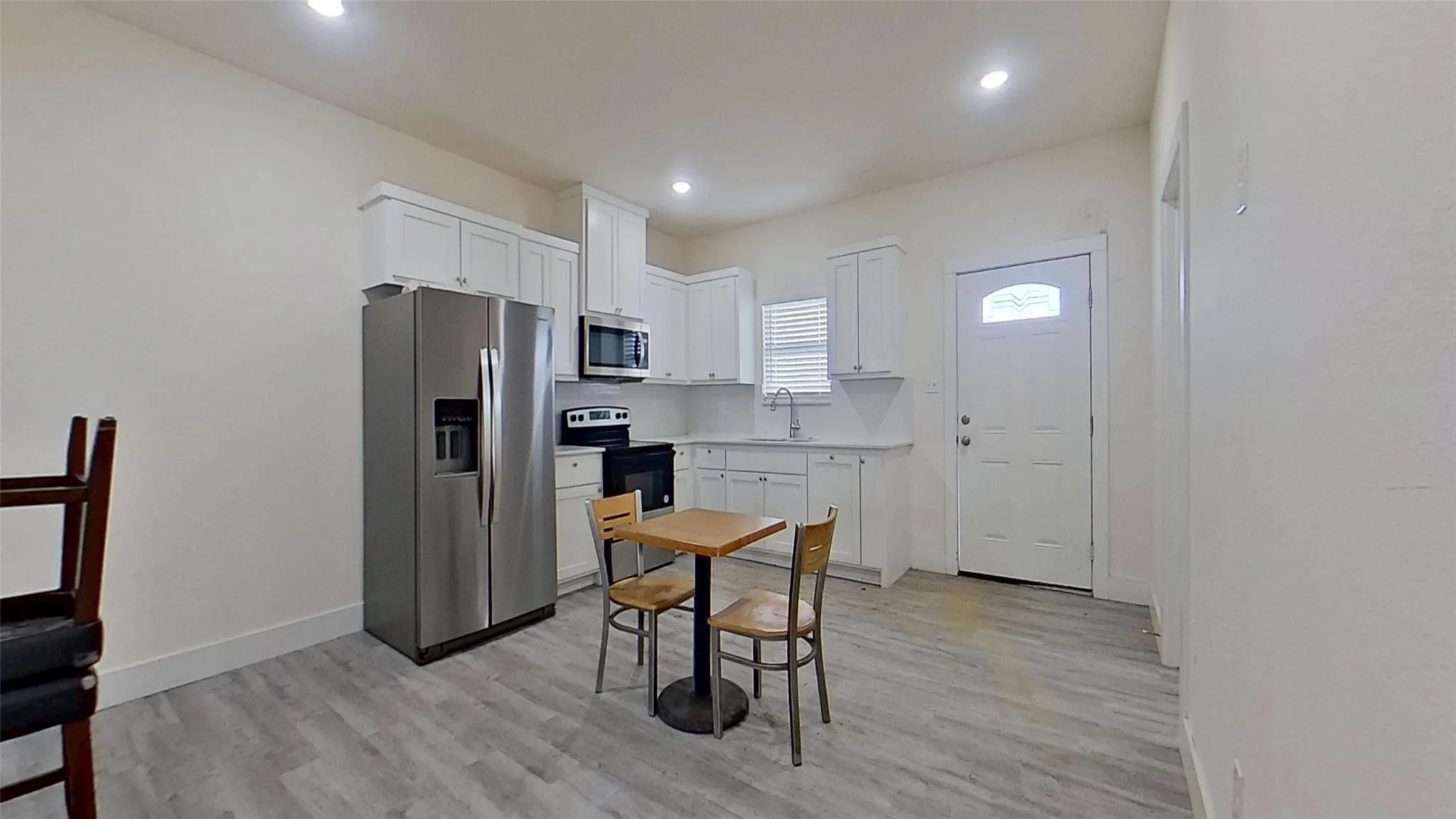 White cabinetry, white countertops, stainless steel appliances, wood-finish flooring, and a window with blinds