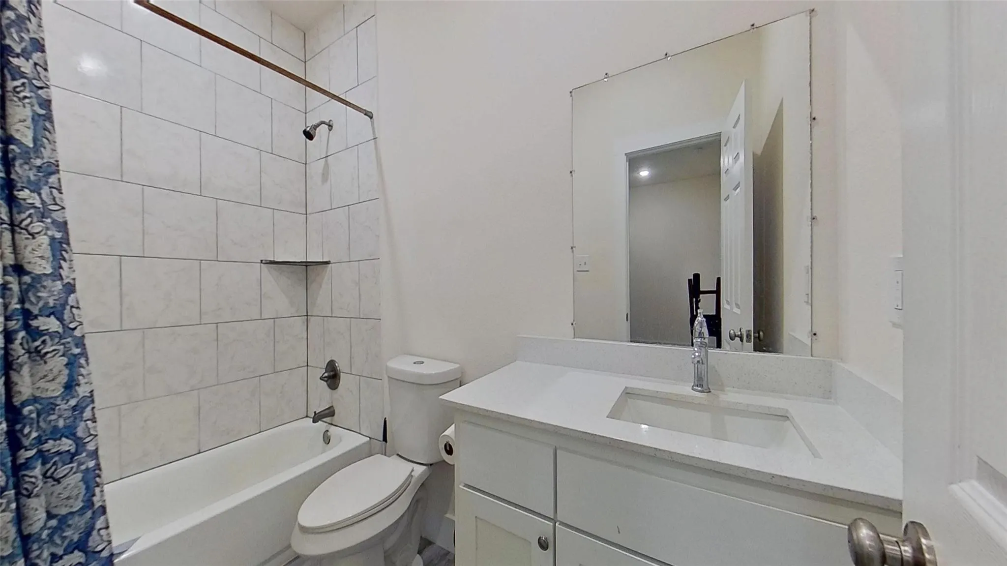 White tile shower surround with a built-in shelf, white bathtub, white toilet, white vanity with an integrated rectangular sink, and a large wall-mounted mirror