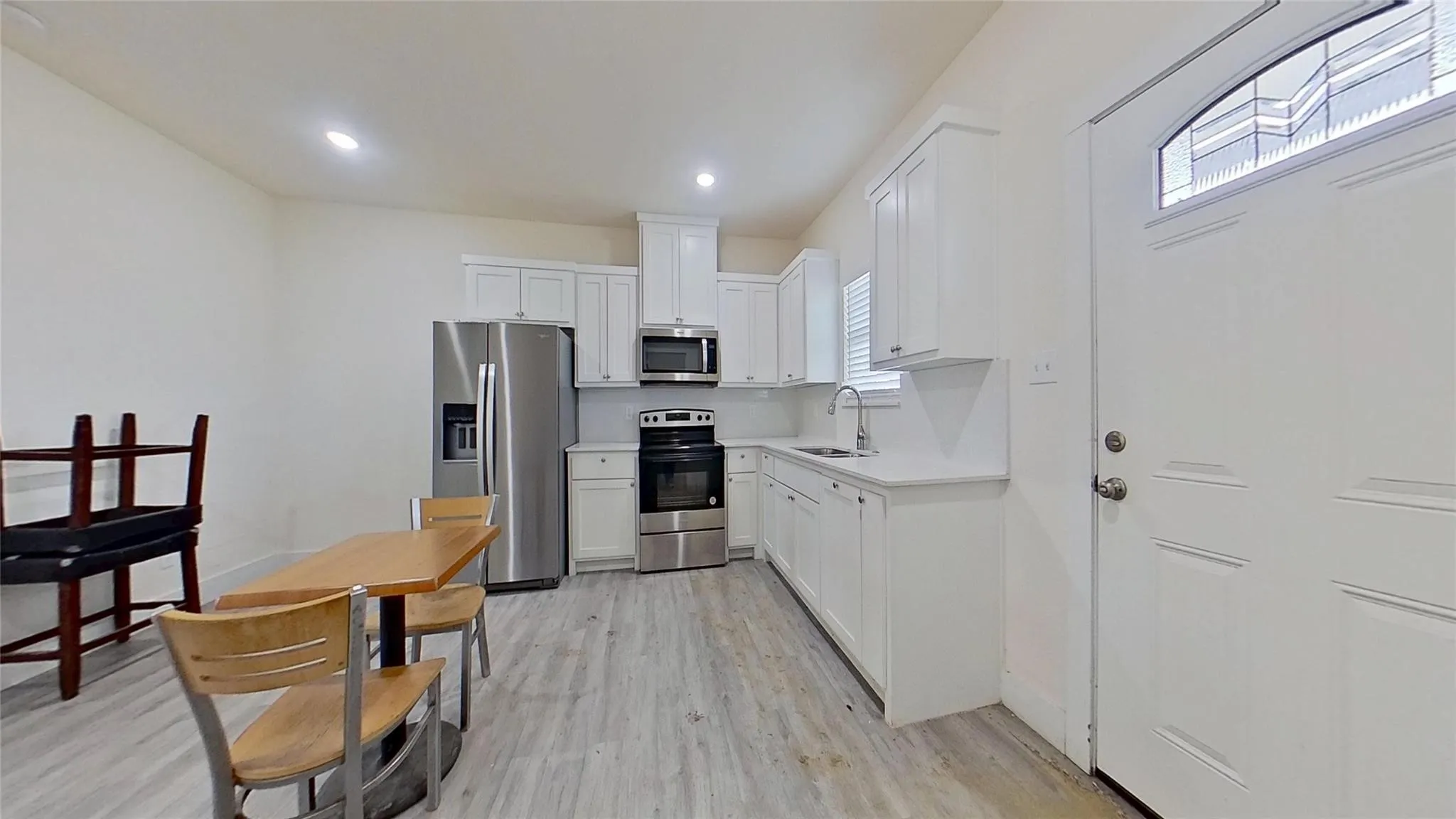 Kitchen with wood-finish flooring, white cabinetry, stainless steel appliances, and recessed lighting