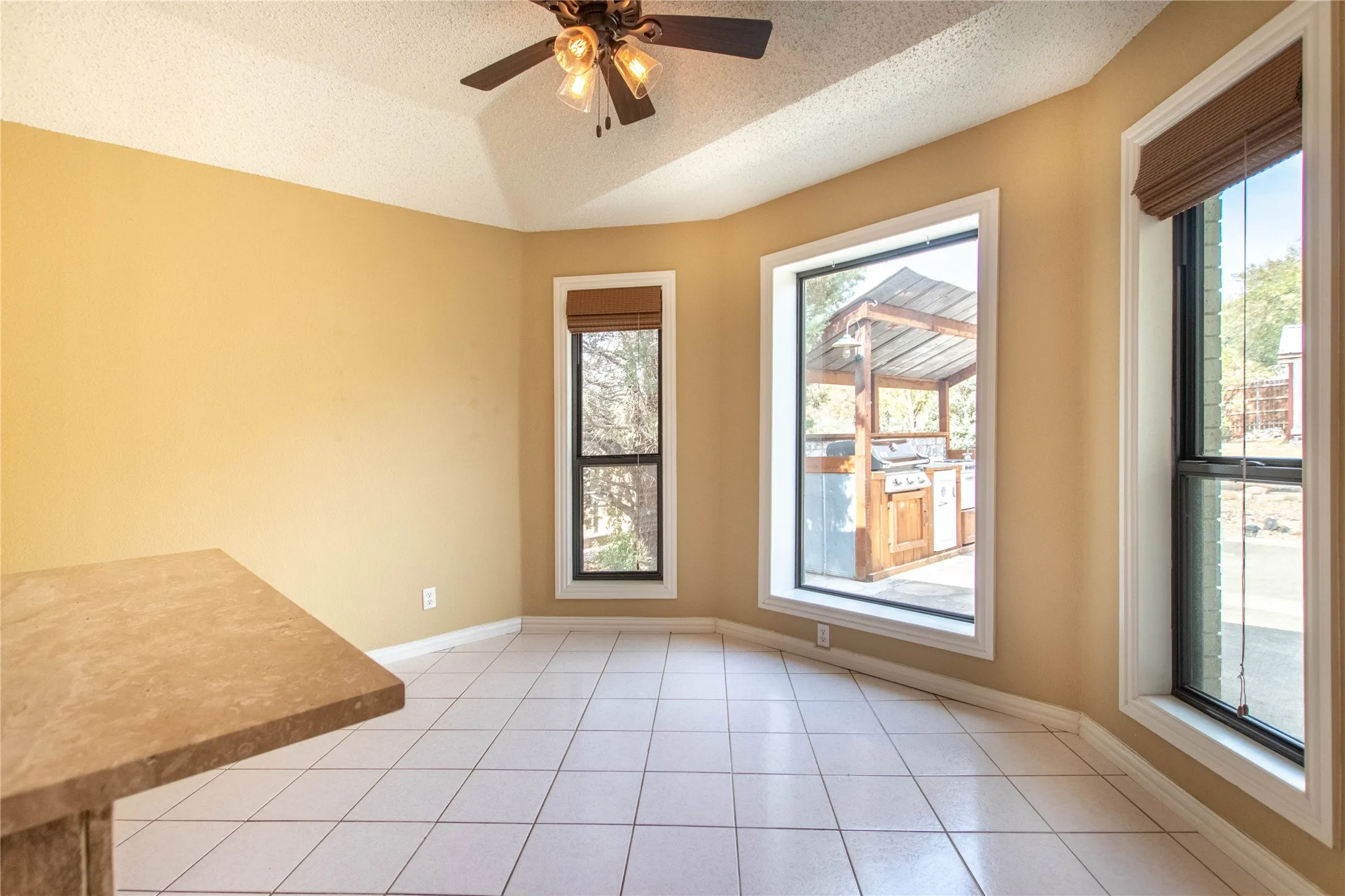 Slanted vaulted ceiling with a ceiling fan, bay window configuration, tile flooring, and a built-in countertop