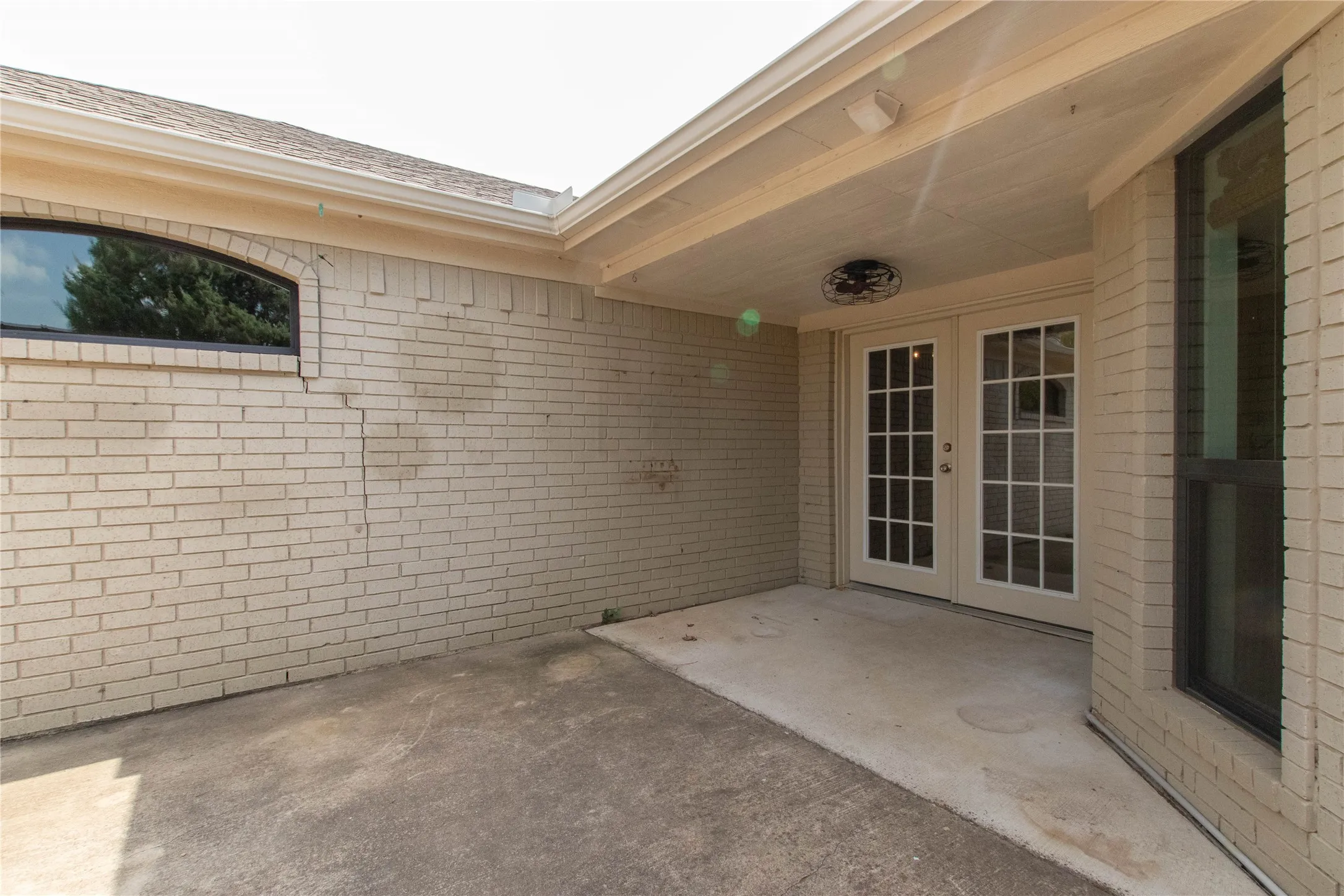 Covered patio area with concrete flooring, brick exterior, and French doors
