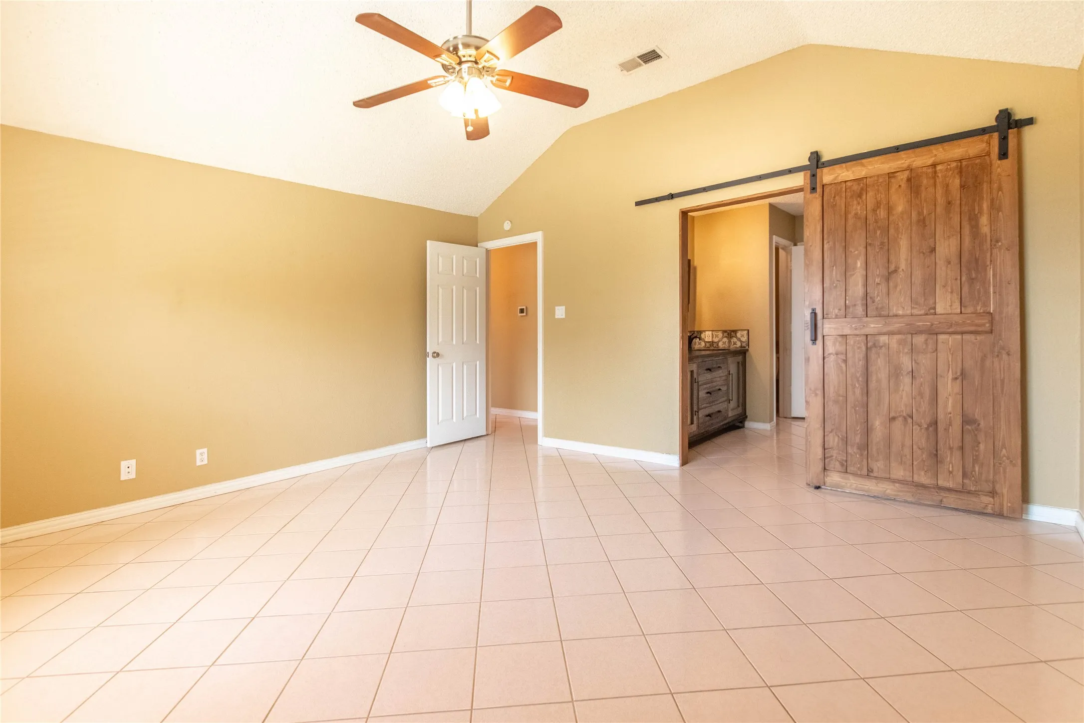 Vaulted ceiling with ceiling fan, tile flooring, solid wood barn door, and built-in vanity with patterned tile detail