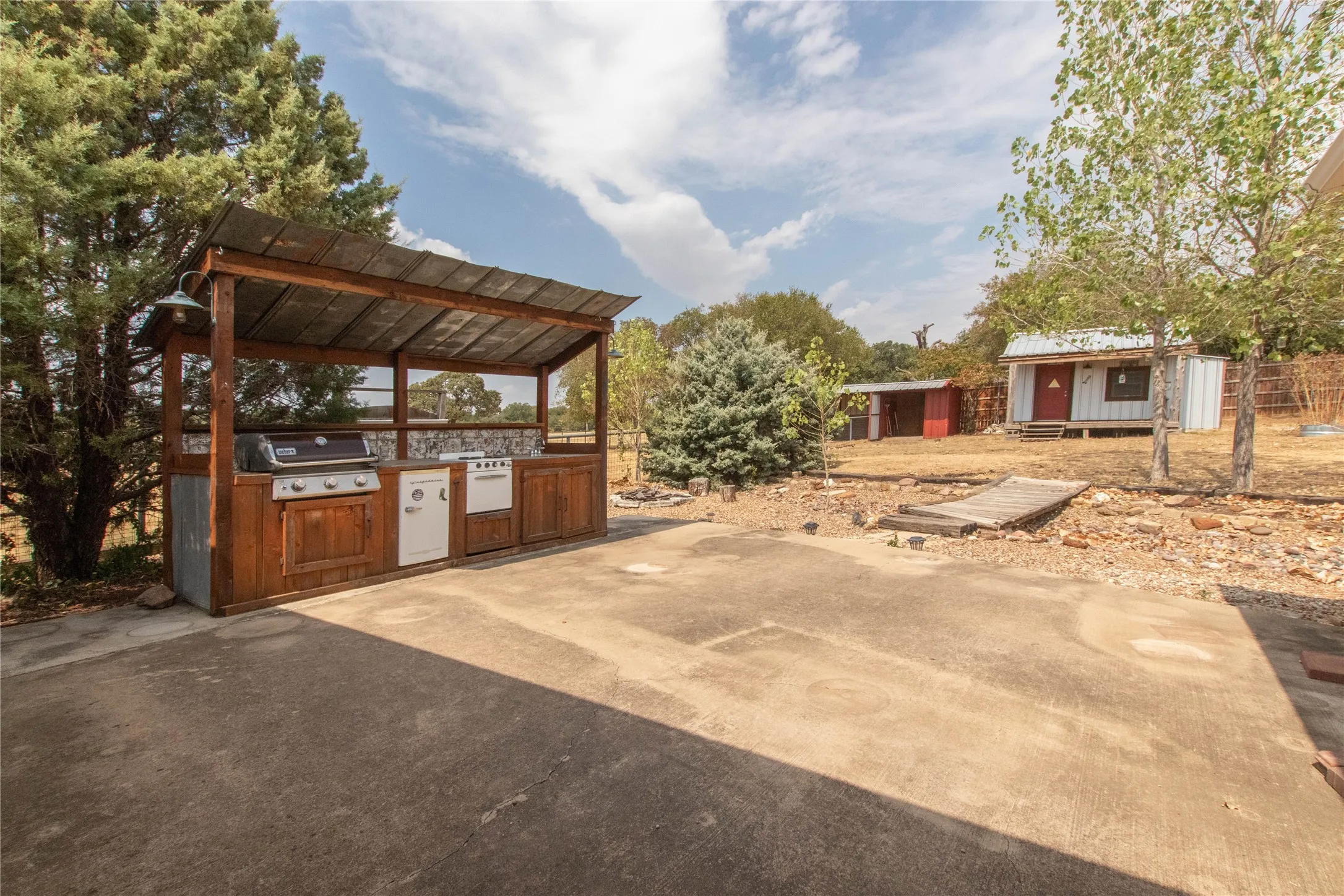 Outdoor kitchen featuring a built-in grill, sink, and wood cabinetry with a metal roof