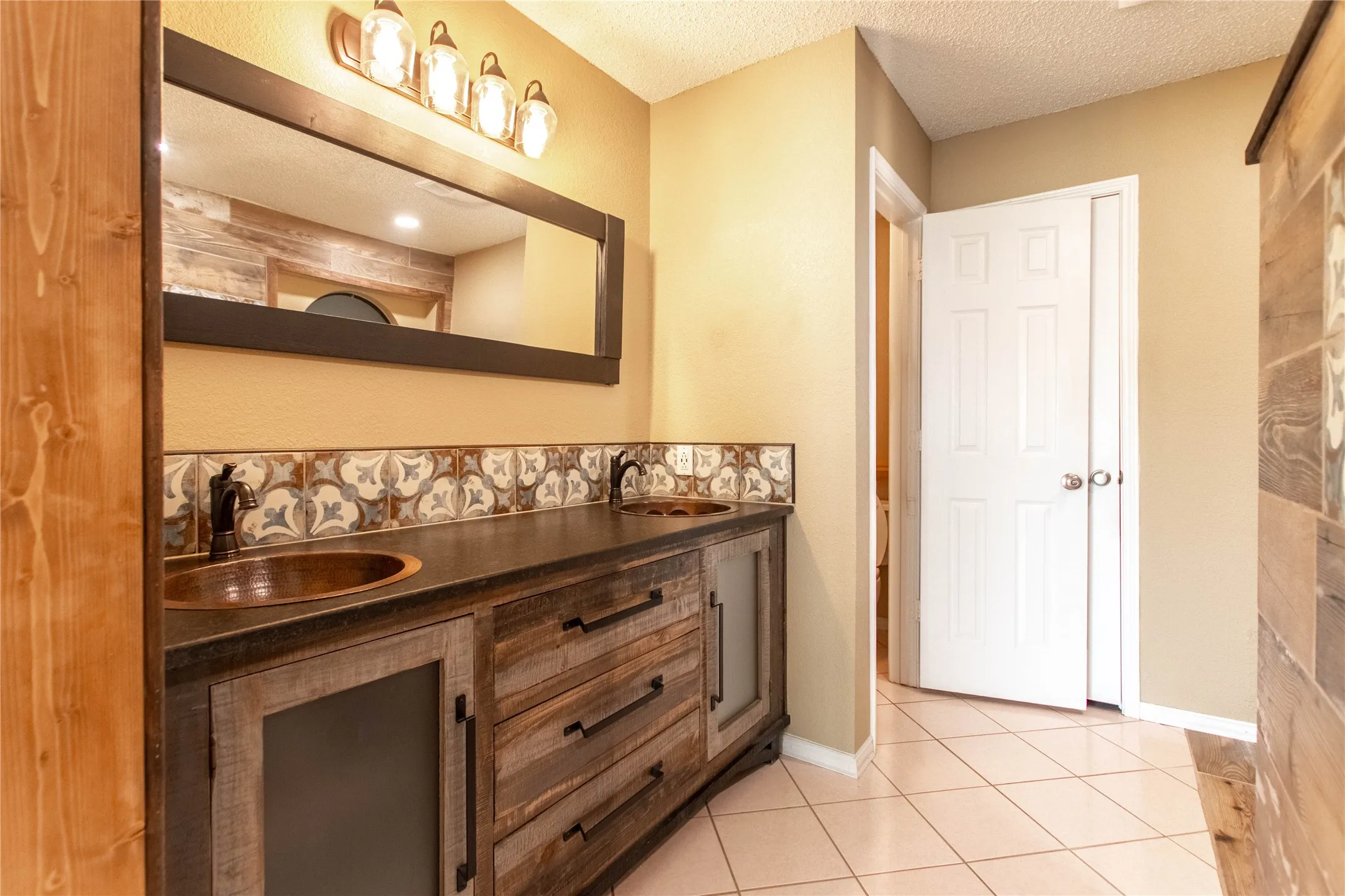 Wood-finish vanity with dual copper vessel sinks, patterned tile backsplash, and a contemporary light fixture