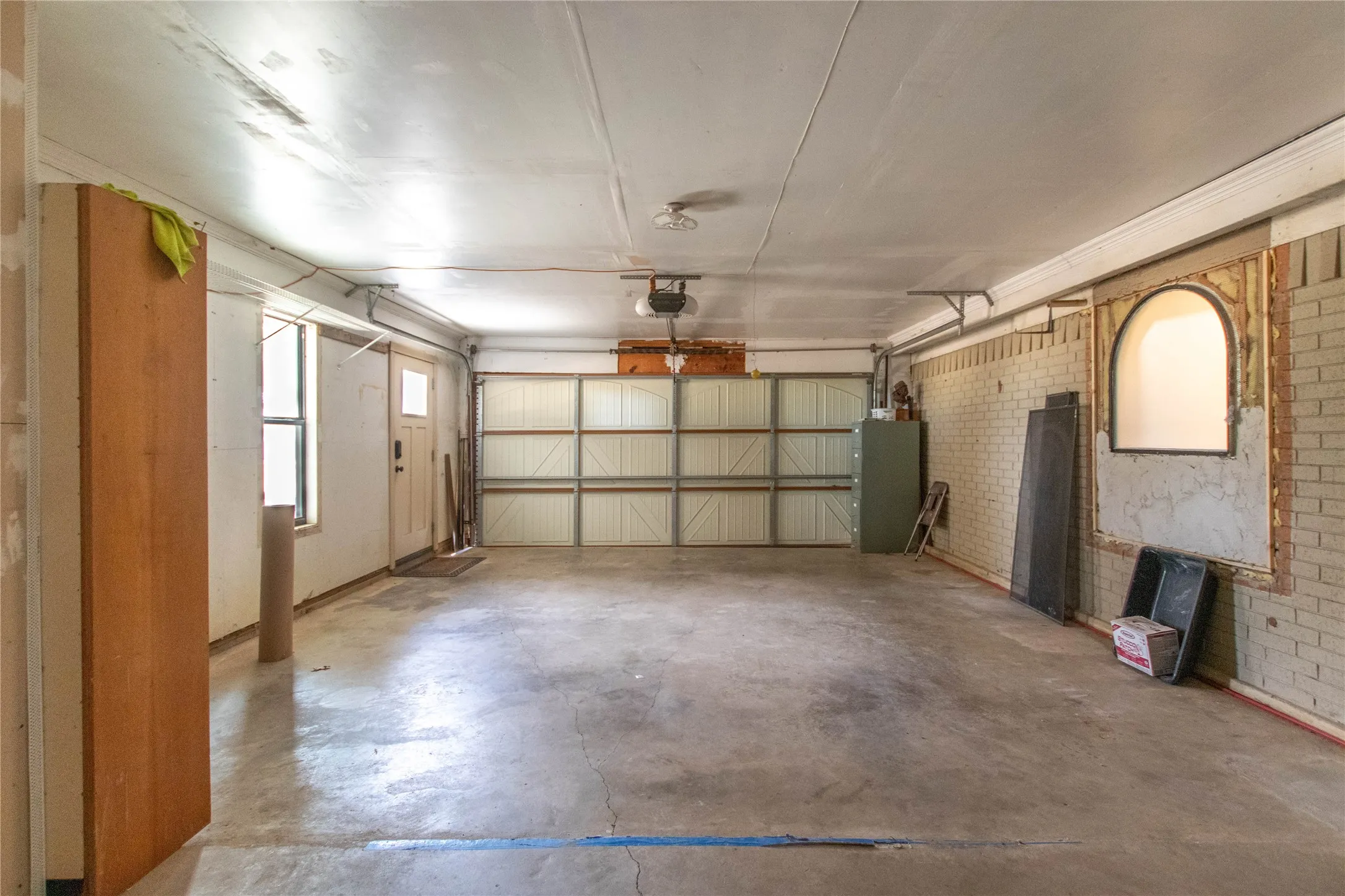 Concrete flooring, automatic garage door, recessed lighting, and a brick wall