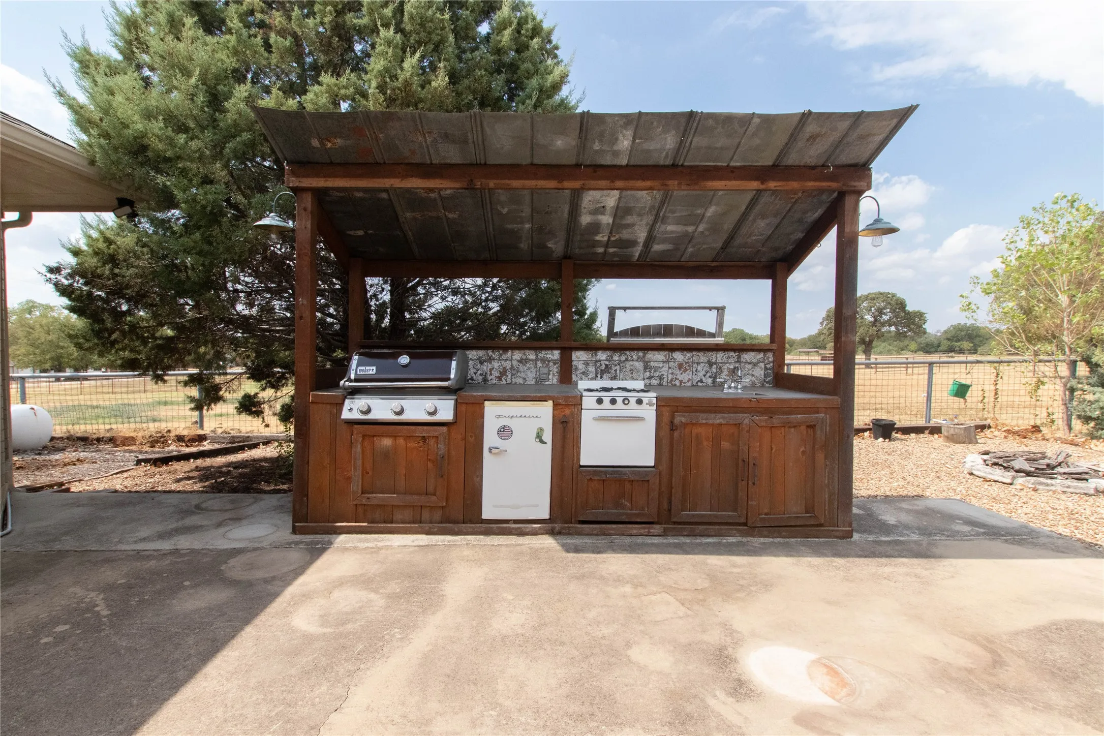 Outdoor kitchen area featuring a corrugated metal roof, wood-finish cabinetry, built-in grill, and a freestanding range