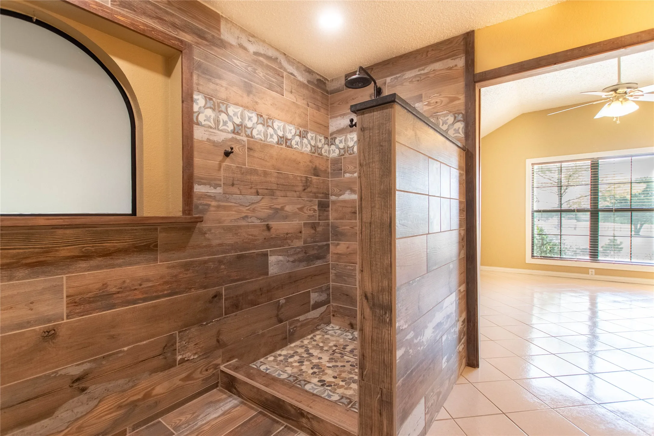 Walk-in shower with wood-finish tile, decorative accent tile, and a pebble-finish floor