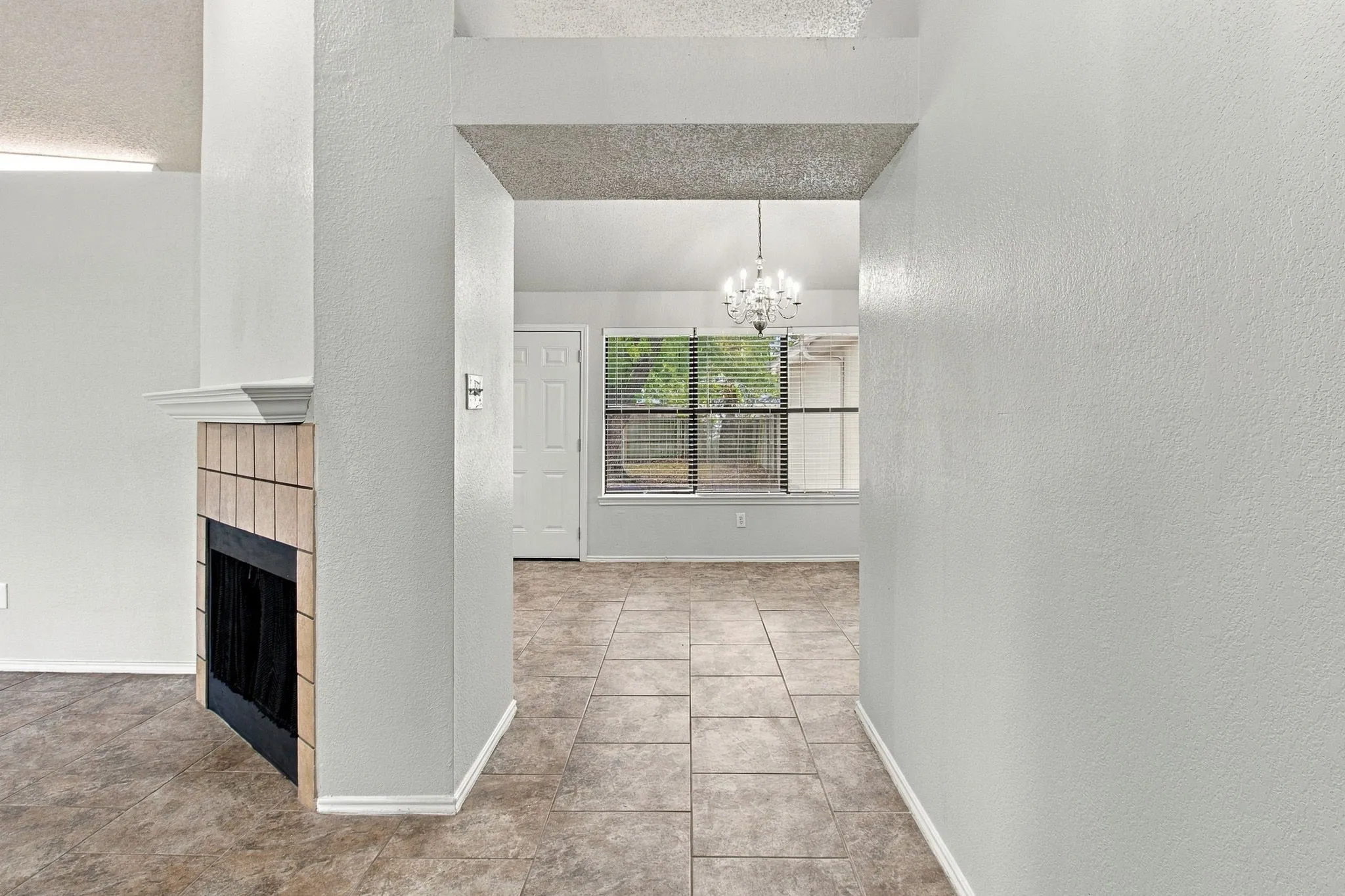 Tile flooring throughout, a tiled fireplace with a mantel, and a window with blinds