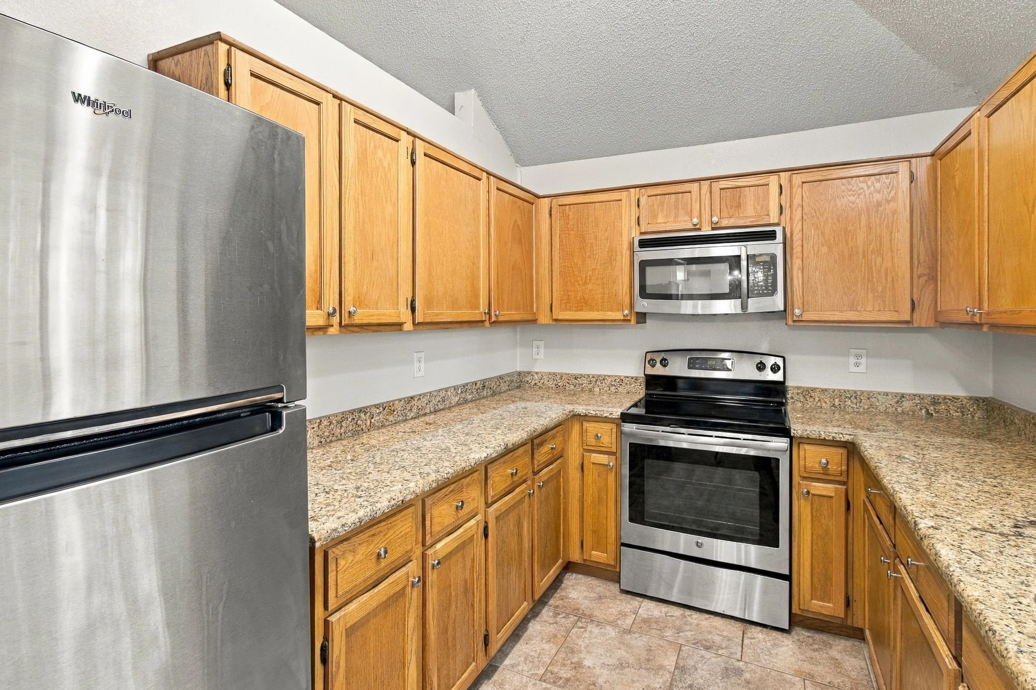 Kitchen featuring wood cabinetry, stainless steel appliances, speckled countertops, and tiled flooring