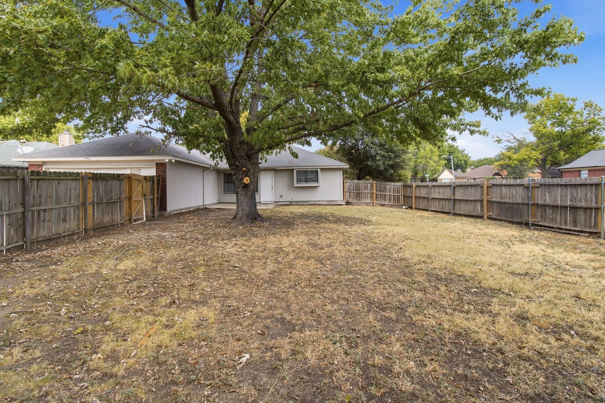 Expansive backyard featuring a mature tree, wood fencing, and a white exterior home with a dark roof