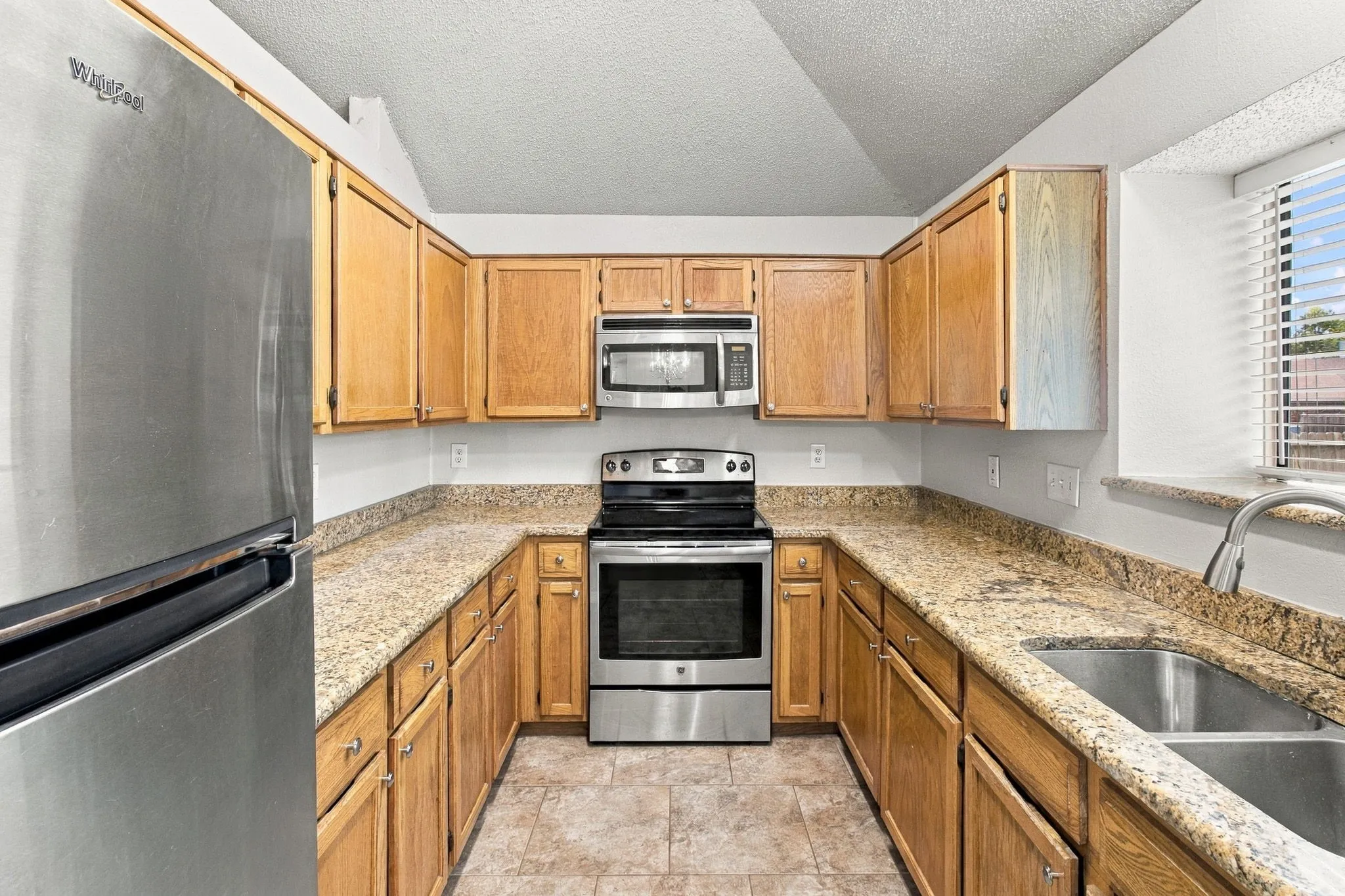 U-shaped kitchen featuring wood cabinetry, stainless steel appliances, speckled countertops, and a double basin sink