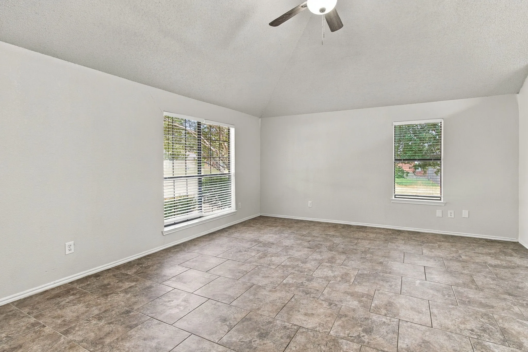 Vaulted ceiling, ceiling fan with integrated lighting, tiled flooring, and multiple windows