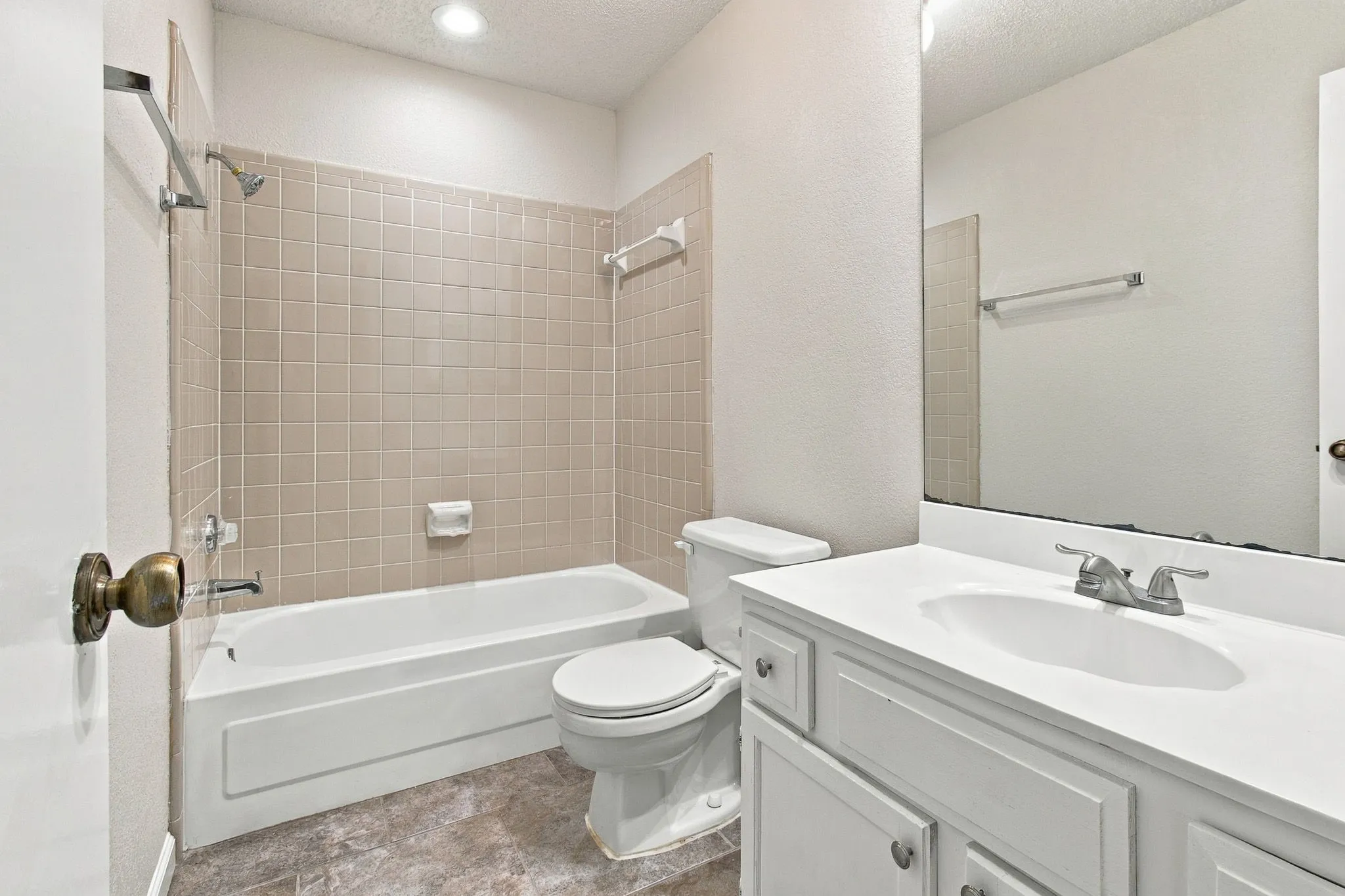 Bathroom featuring a vanity with an integrated sink, a large mirror, a toilet, a bathtub, and tiled shower walls