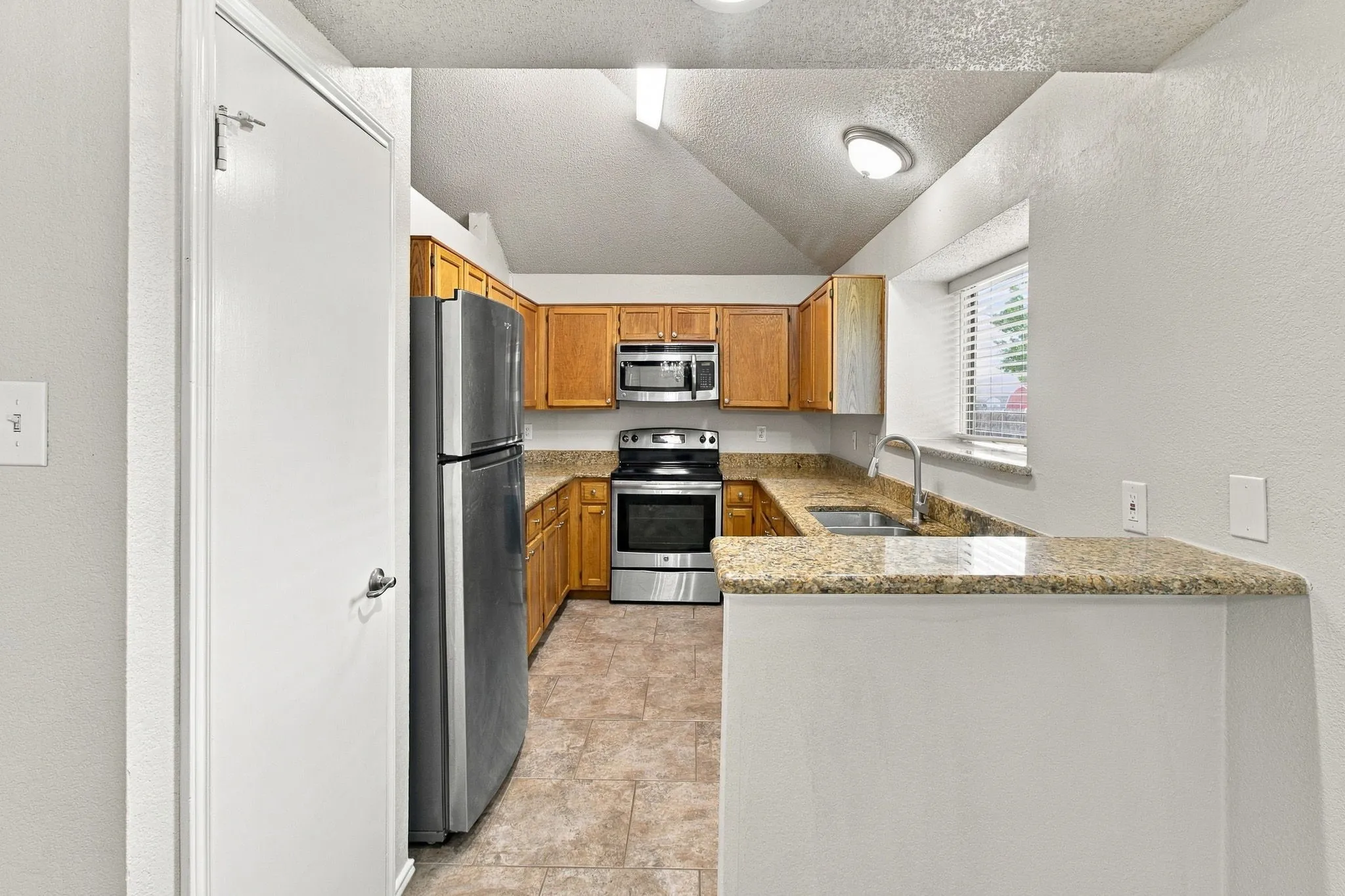 Kitchen featuring wood cabinetry, stainless steel appliances, a double basin sink, stone countertops, and tile flooring