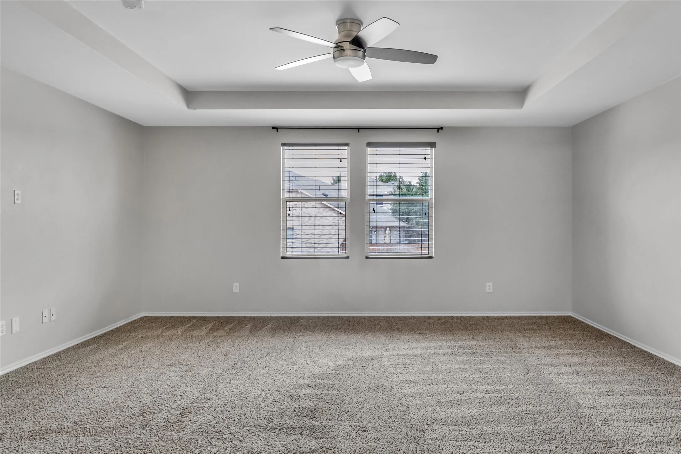 Recessed tray ceiling with a modern ceiling fan, neutral carpet flooring, and dual windows