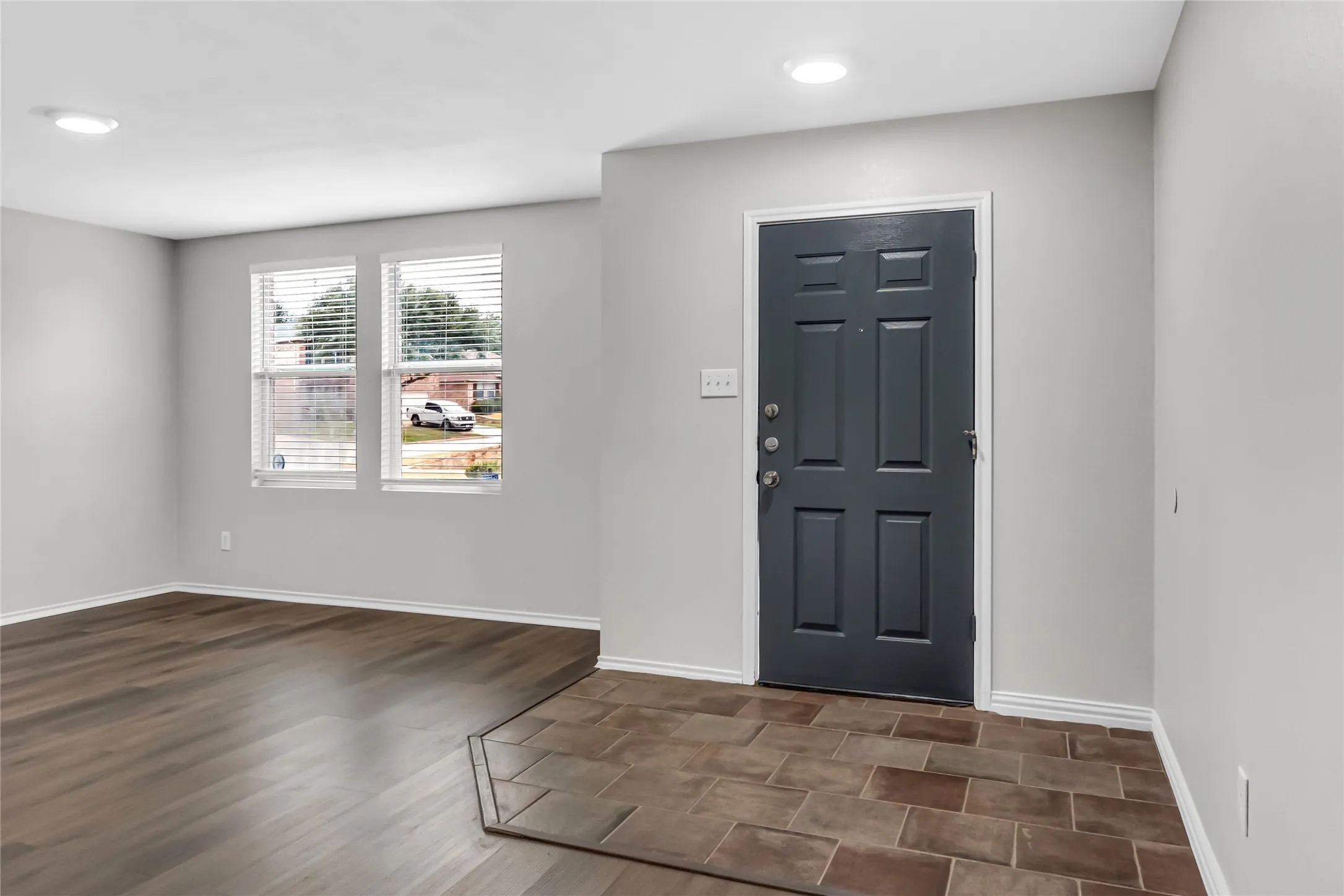 Two large windows, recessed ceiling lighting, wood-finish flooring, and a paneled entry door