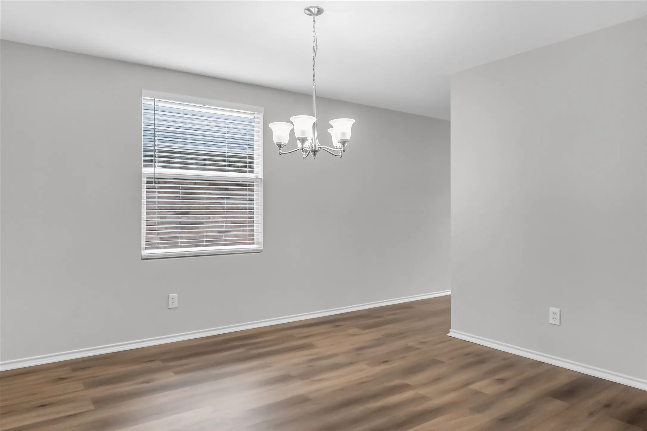 Wood-finish flooring, single window with blinds, overhead chandelier with three sconces, and light gray wall paint