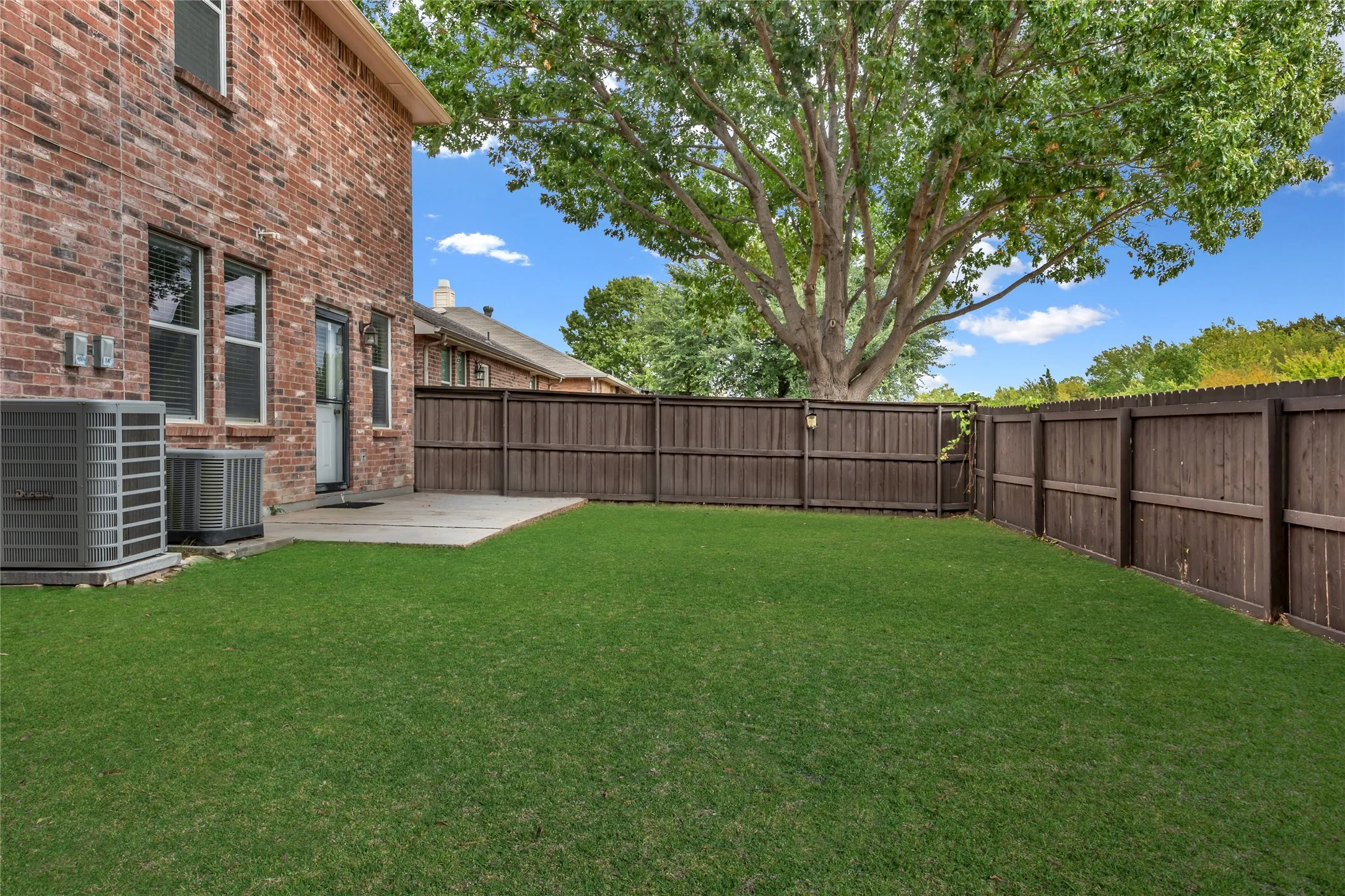 Expansive lawn with mature tree, private wood fencing, and a concrete patio