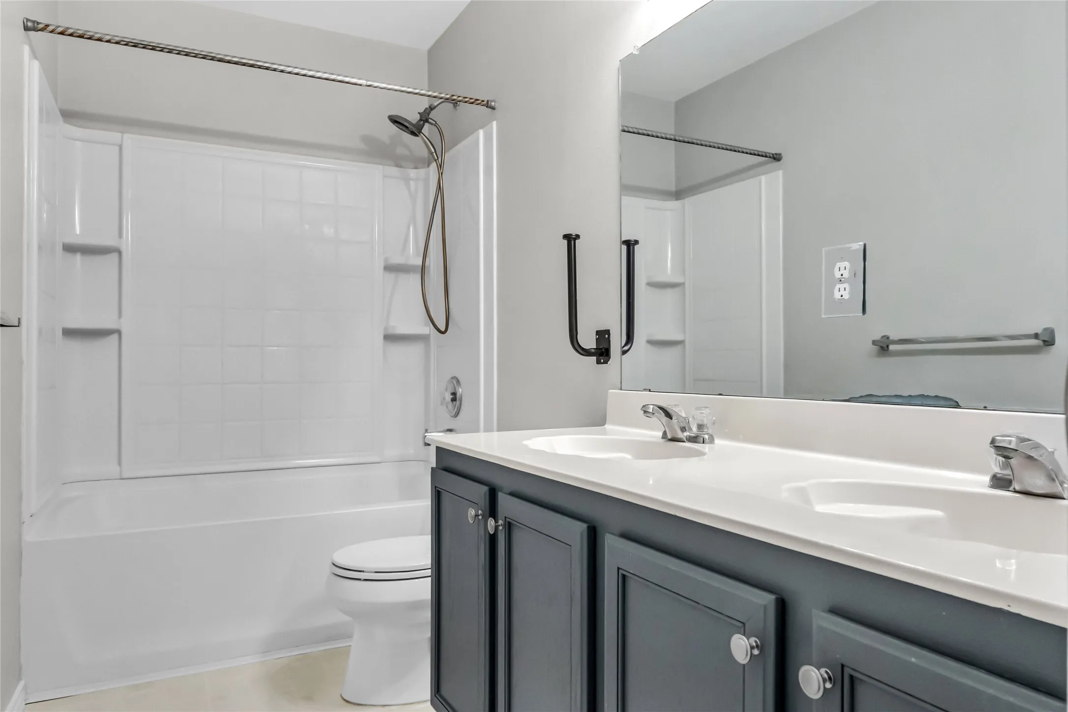 White tub and shower combination with built-in shelving, dual sink vanity with white countertop, and dark cabinetry with brushed nickel hardware