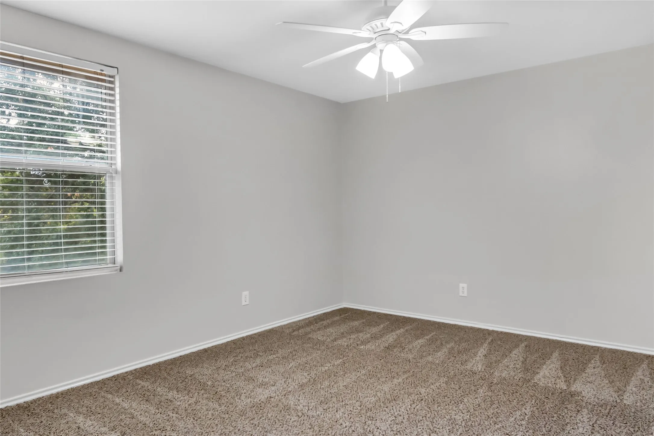 Neutral tone wall paint, textured carpeting, window with blinds, and a ceiling fan with integrated lighting