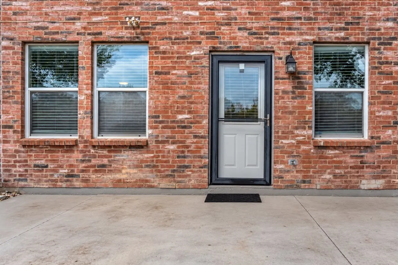 Brick exterior with a concrete patio, white-framed windows, and a storm door