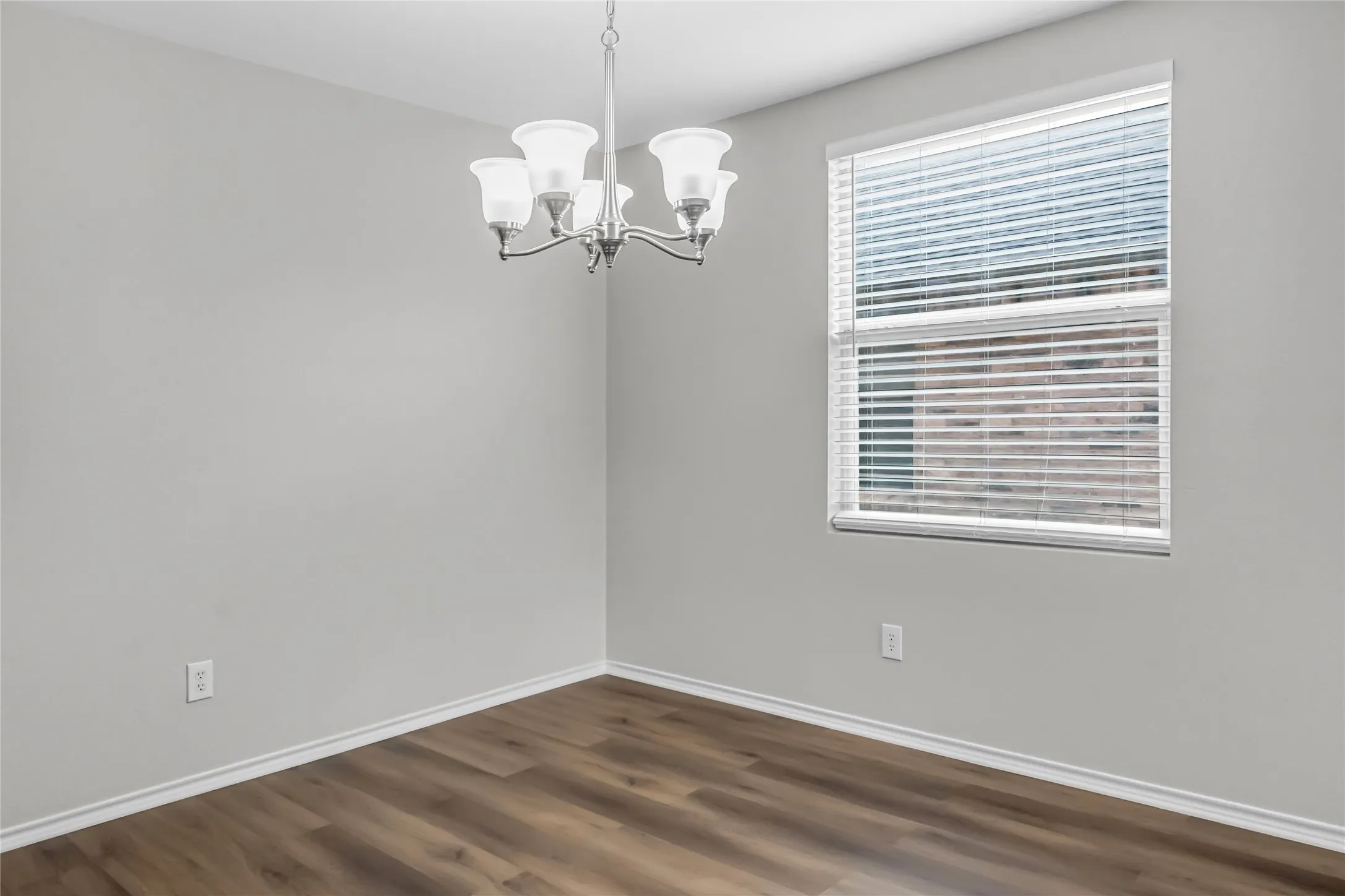 Wood-finish flooring, single window with blinds, and ceiling-mounted chandelier