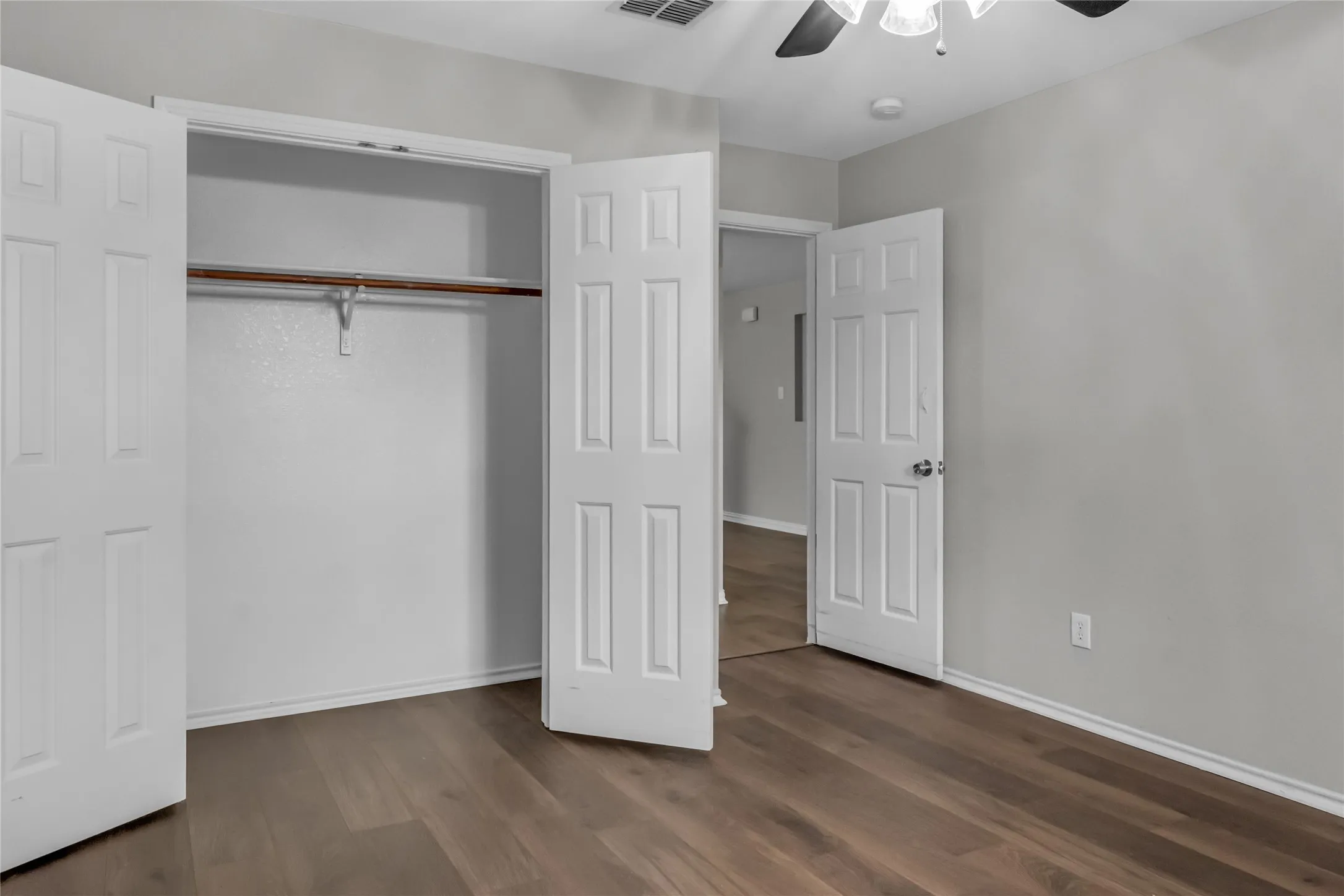 Wood-finish flooring, ceiling fan with light fixture, and a built-in closet with hanging rod