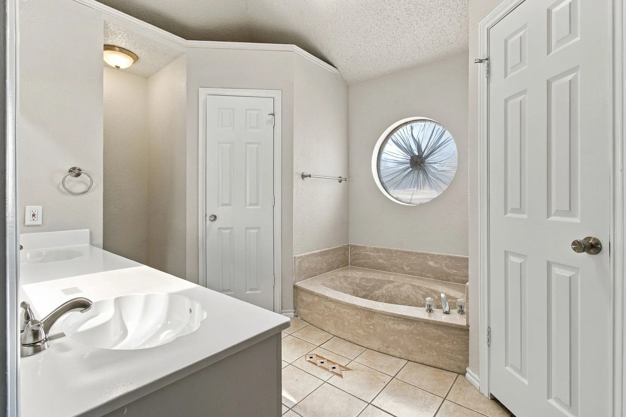 Built-in soaking tub with a tiled surround, circular window, single vanity with integrated sink, and tiled flooring