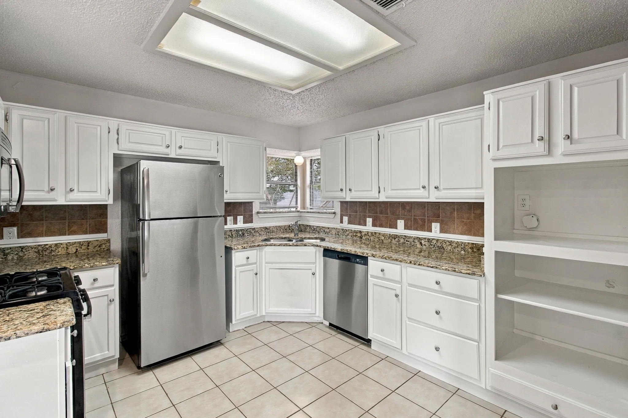 White cabinetry with silver-tone hardware, tile flooring, built-in shelving, stainless steel appliances, and a tiled backsplash