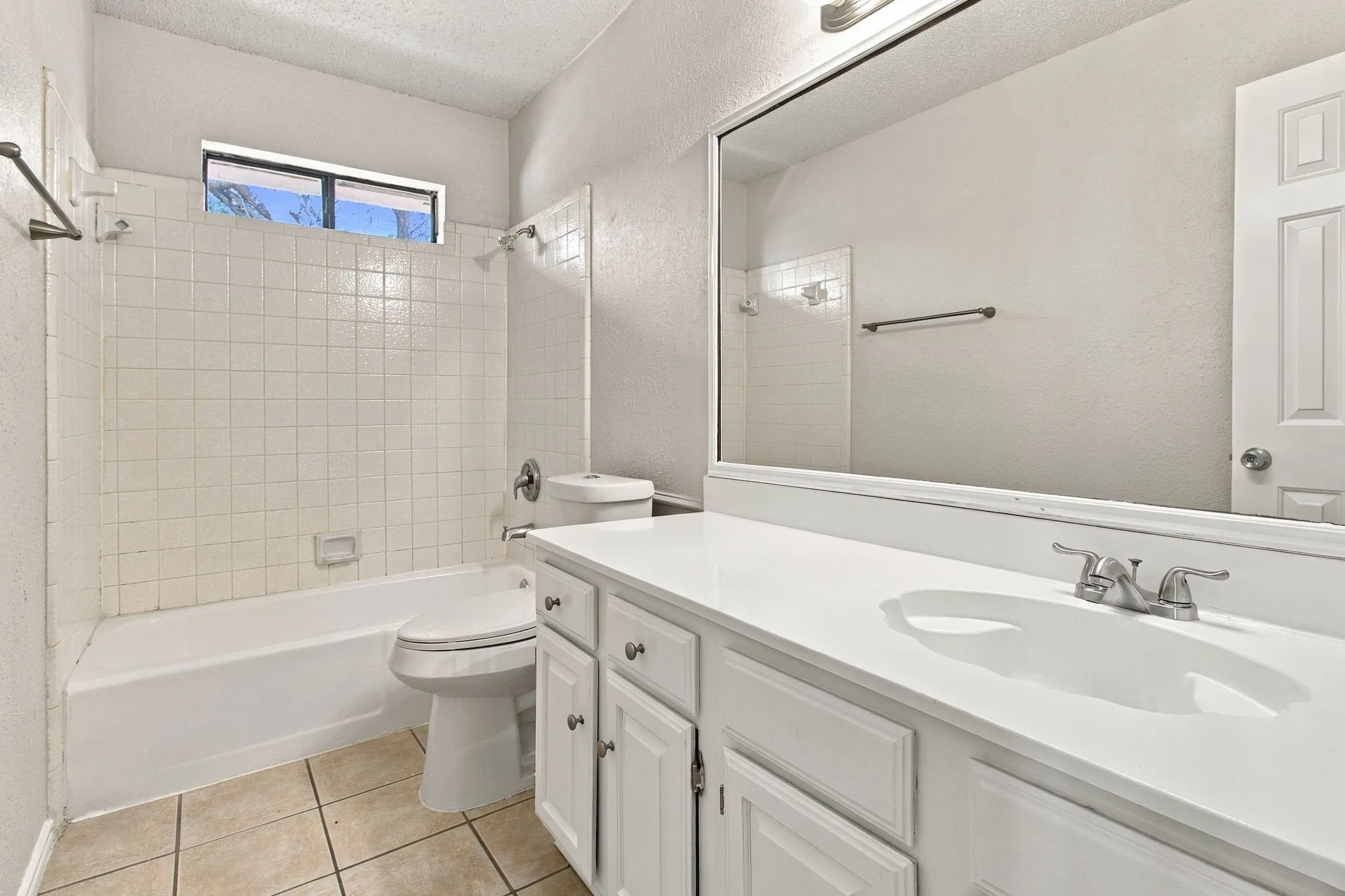 White tile flooring, single vanity with integrated sink, white cabinetry, shower/tub combination with subway tile surround, and a mirror