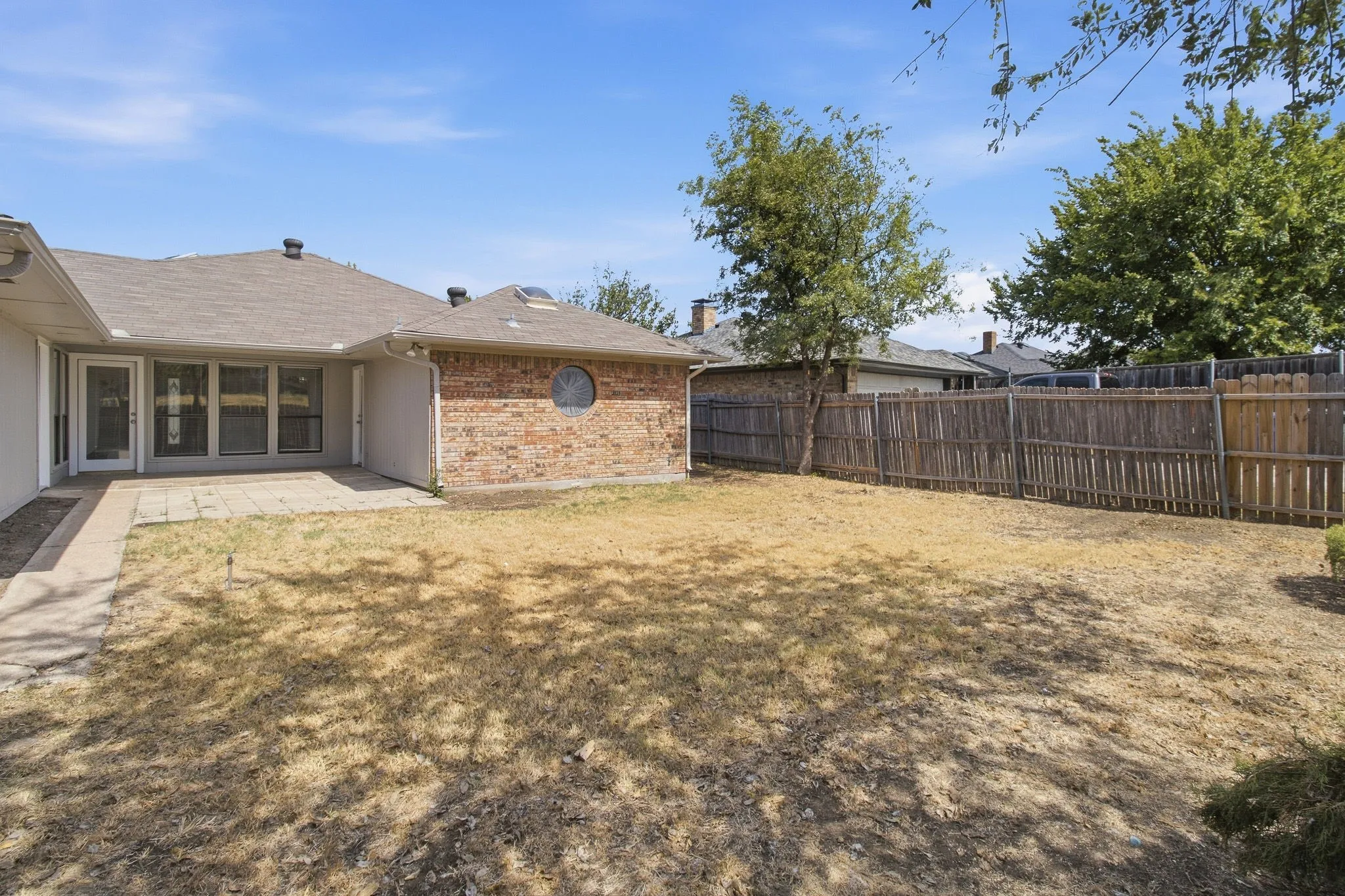 Expansive backyard featuring a wood fence, concrete patio, and a brick exterior with a circular window